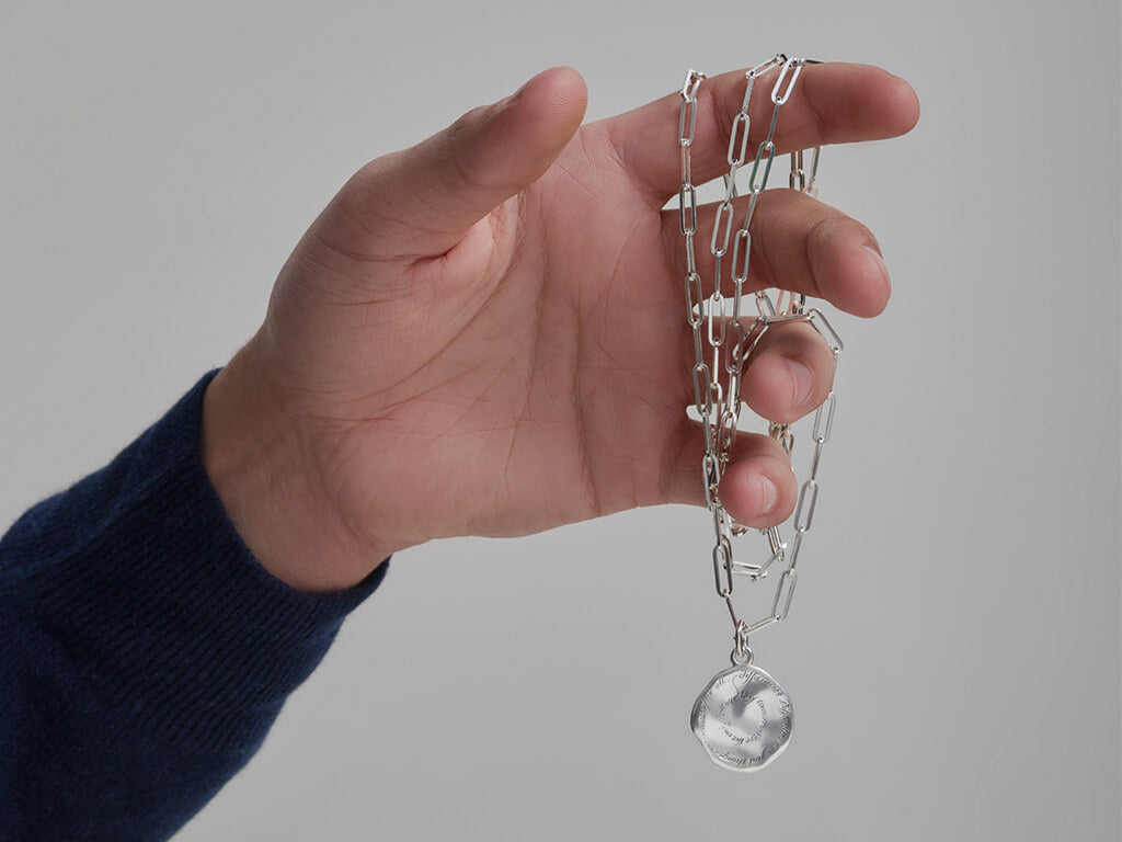 Hand holding silver Quote pendant on a chain.