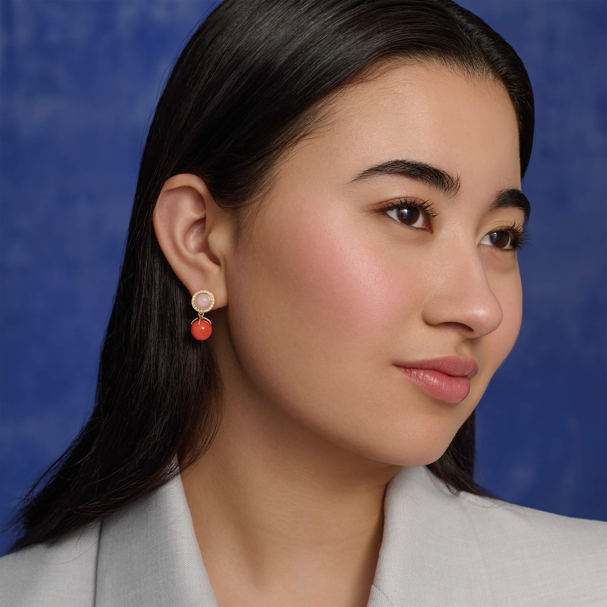 Model wearing handcrafted yellow gold earring drops with an intricate design with a coral bead at the bottom.