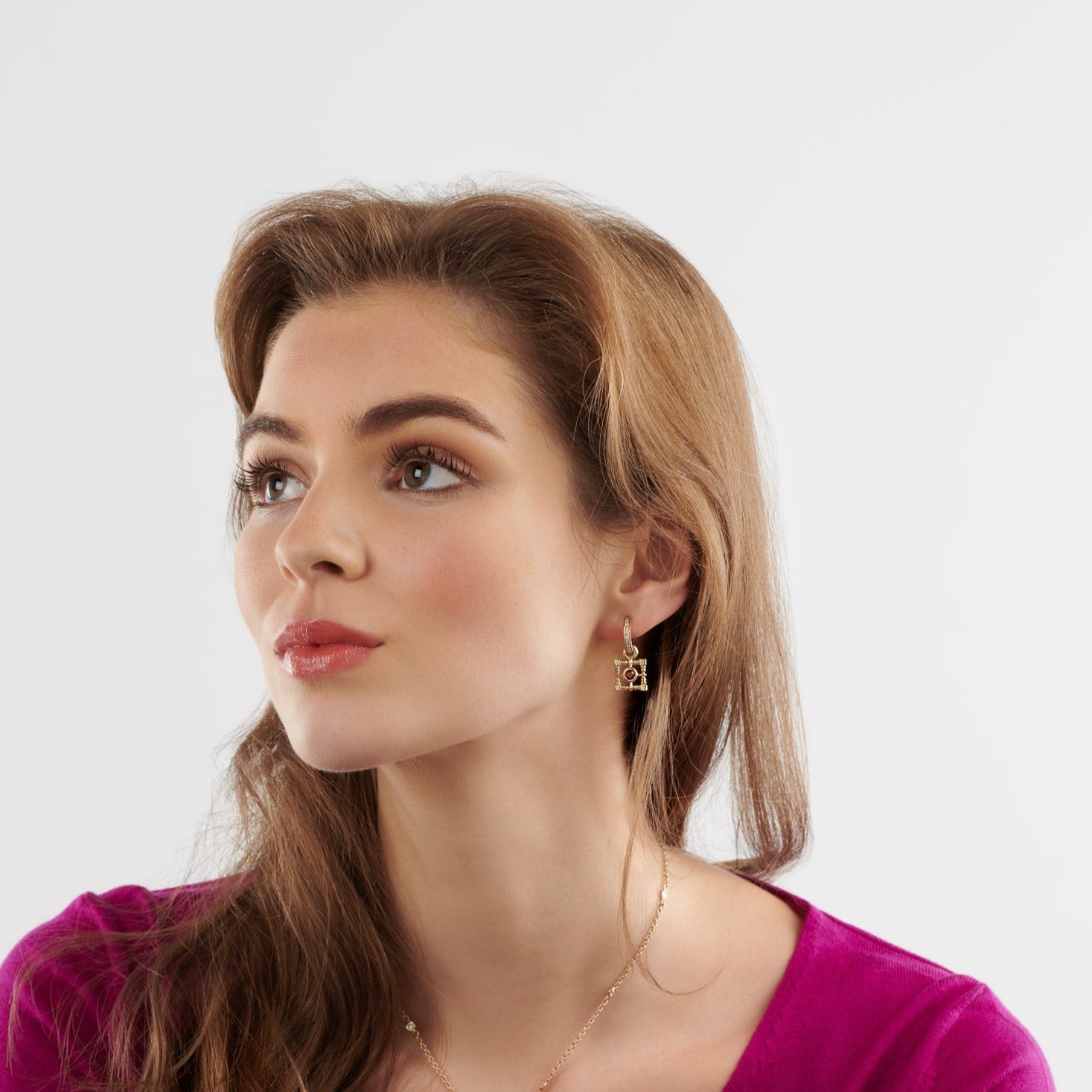 Model wearing handcrafted earring drops in precious metal featuring a square-shaped frame with a central precious stone.