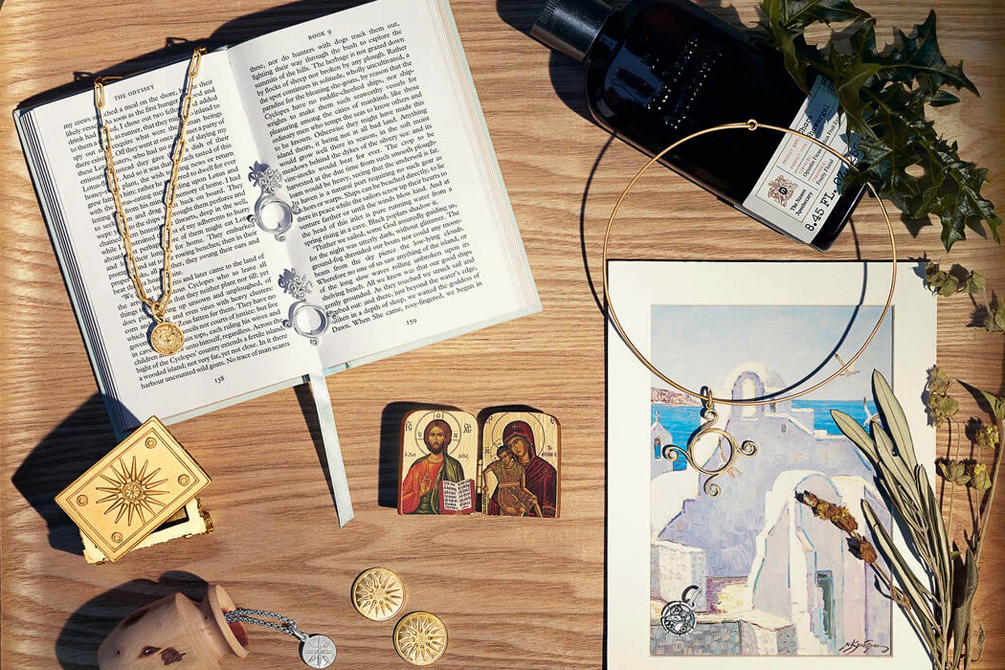 Still life with Greek Still life. From left : Octopus Medallion yellow gold, Star of Vergina Medallion silver, Pallas Athena Double Earrings Silver, and Athena Necklace Pendant Yellow Gold - Diamond on Calypso hard wire chain yellow gold, Owl Medallion Necklace Pendant Silver. Arranged with postcard form Greece, Greek book.