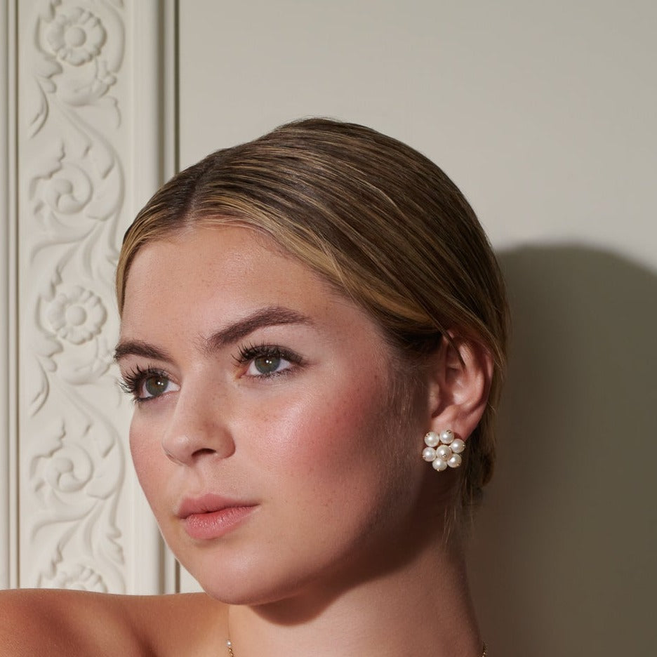 Model wearing handcrafted earrings in 18ct yellow gold featuring a cluster of white pearls. The pearls are interspersed with small diamonds.