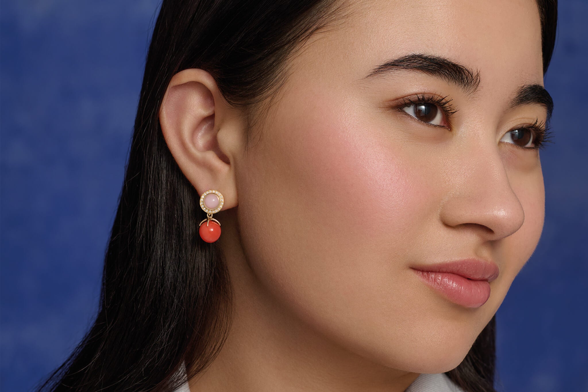 Model wearing handcrafted yellow gold earring drops with an intricate design with a coral bead at the bottom.