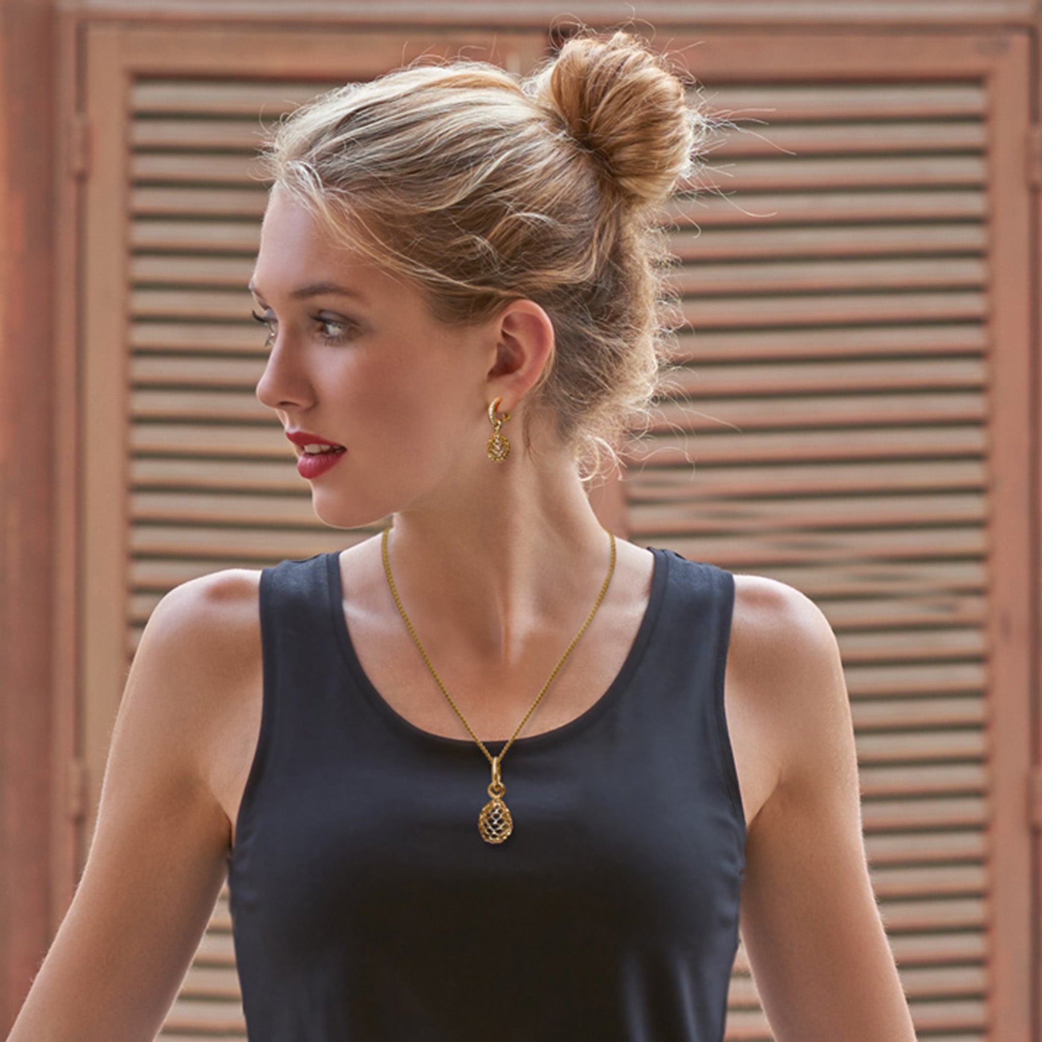 Model wearing a handcrafted yellow gold necklace pendant featuring a pinecone frame.