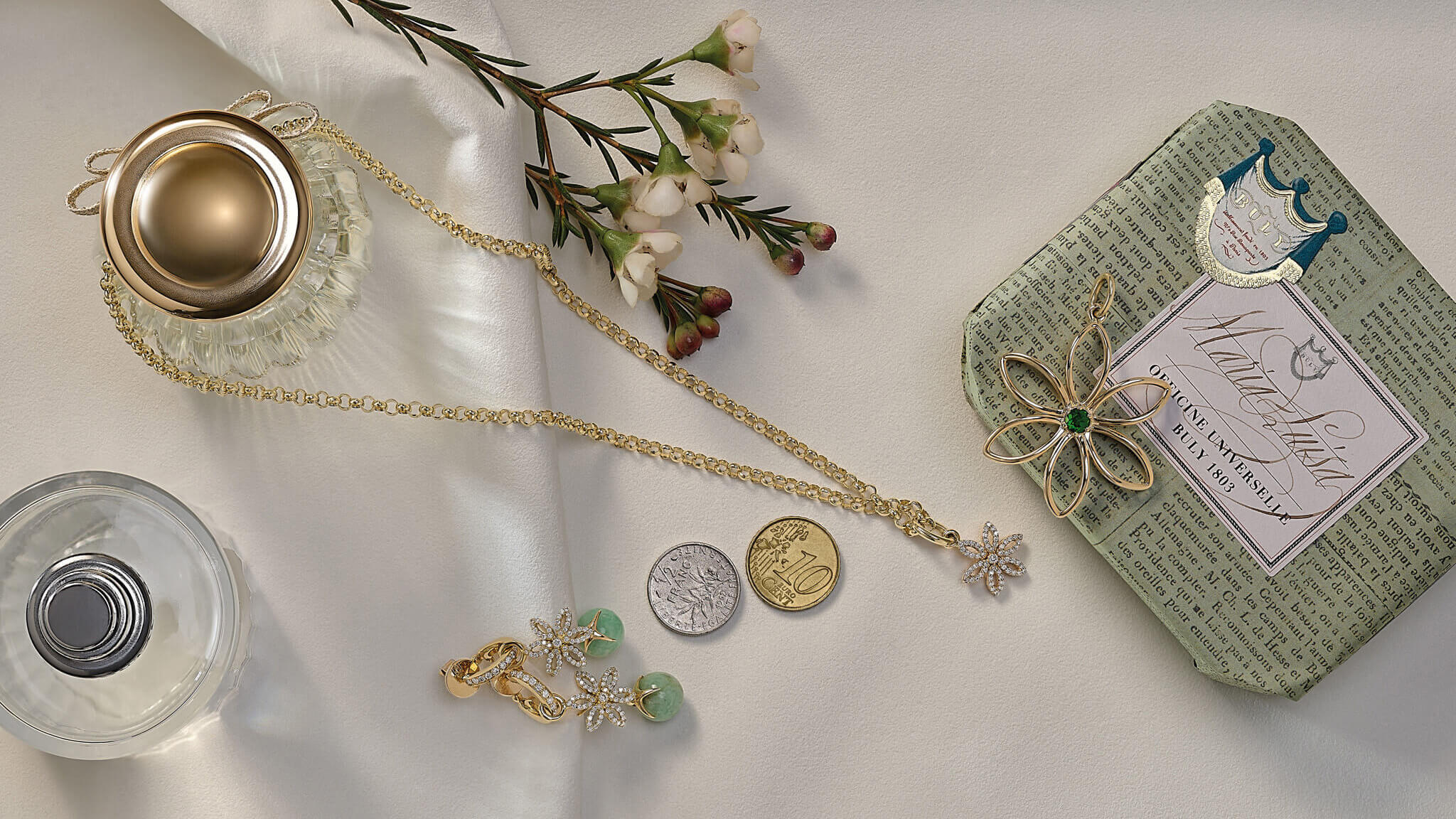Handcrafted necklace pendants laying on a table surrounded by flowers and care products.