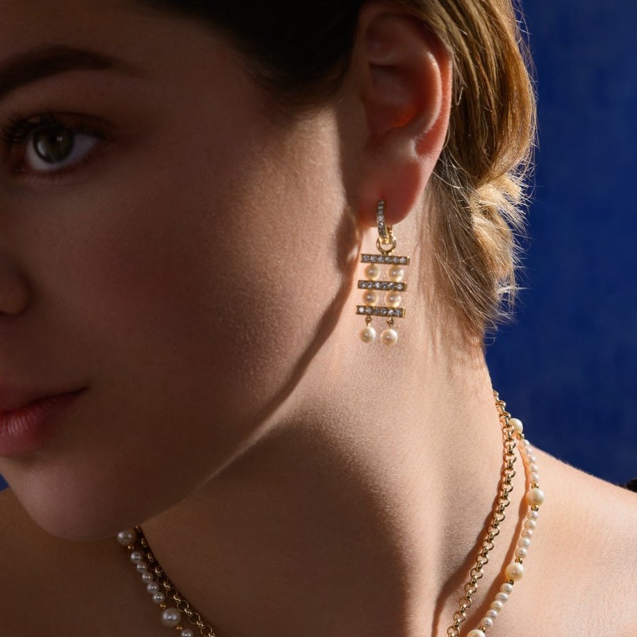 Model wearing handcrafted 18ct yellow gold earring drops with three tiers of pearls separated by delicate gold lines adorned with diamond pav?.