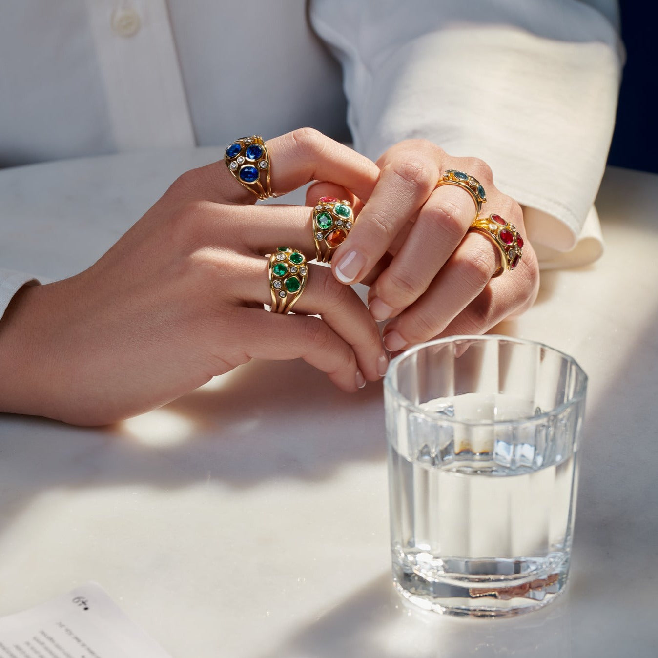 Model wearing five handcrafted 18ct yellow gold rings featuring four precious gemstones and smaller diamonds.