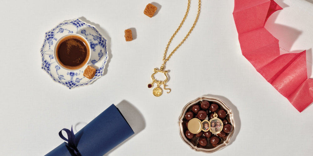 Chatelaine charm holder and Annie locket on white table cloth with Christmas cracker, paper crown, coffee and sugar cubes.