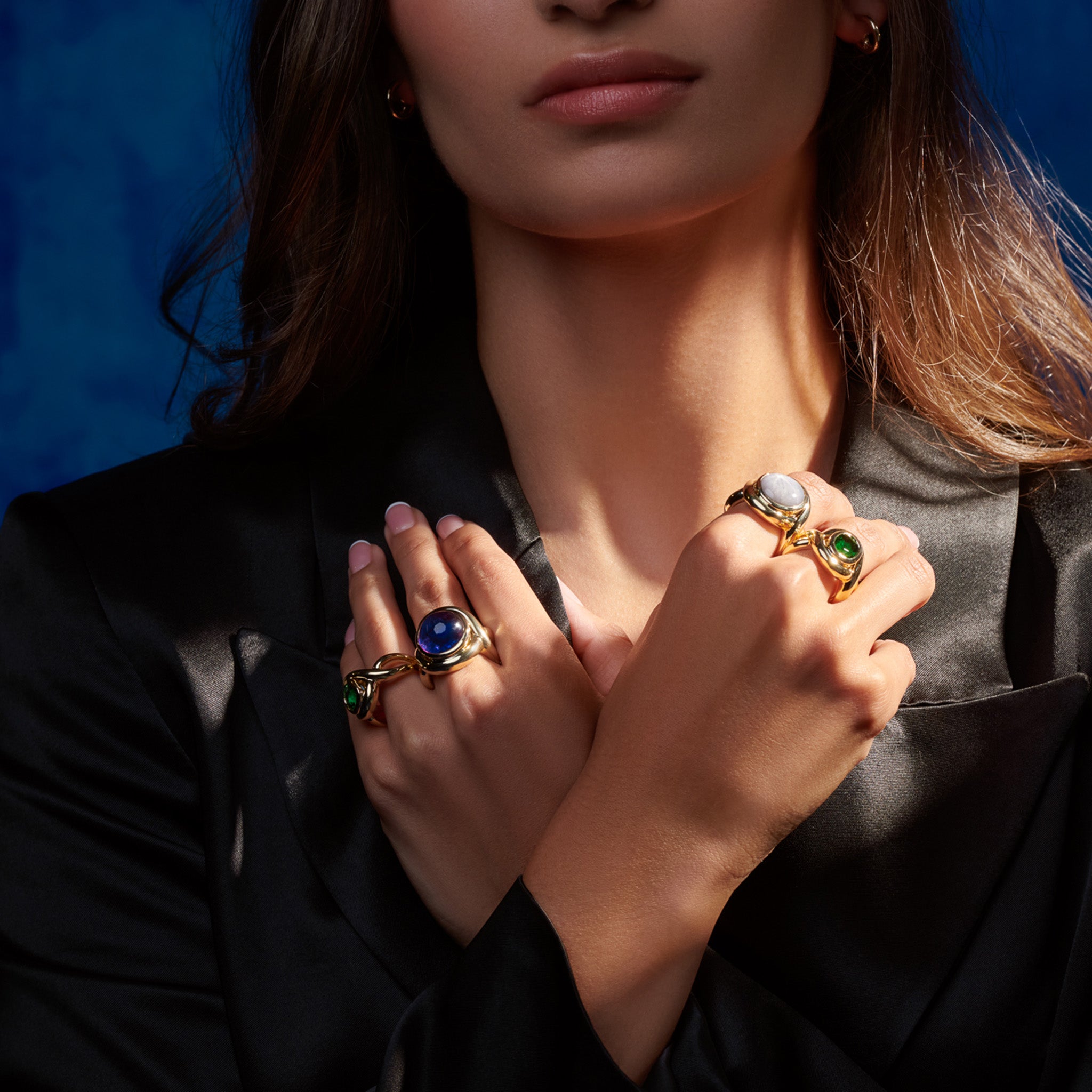 Model wearing handcrafted rings in precious metal featuring curved shanks with round precious stones.