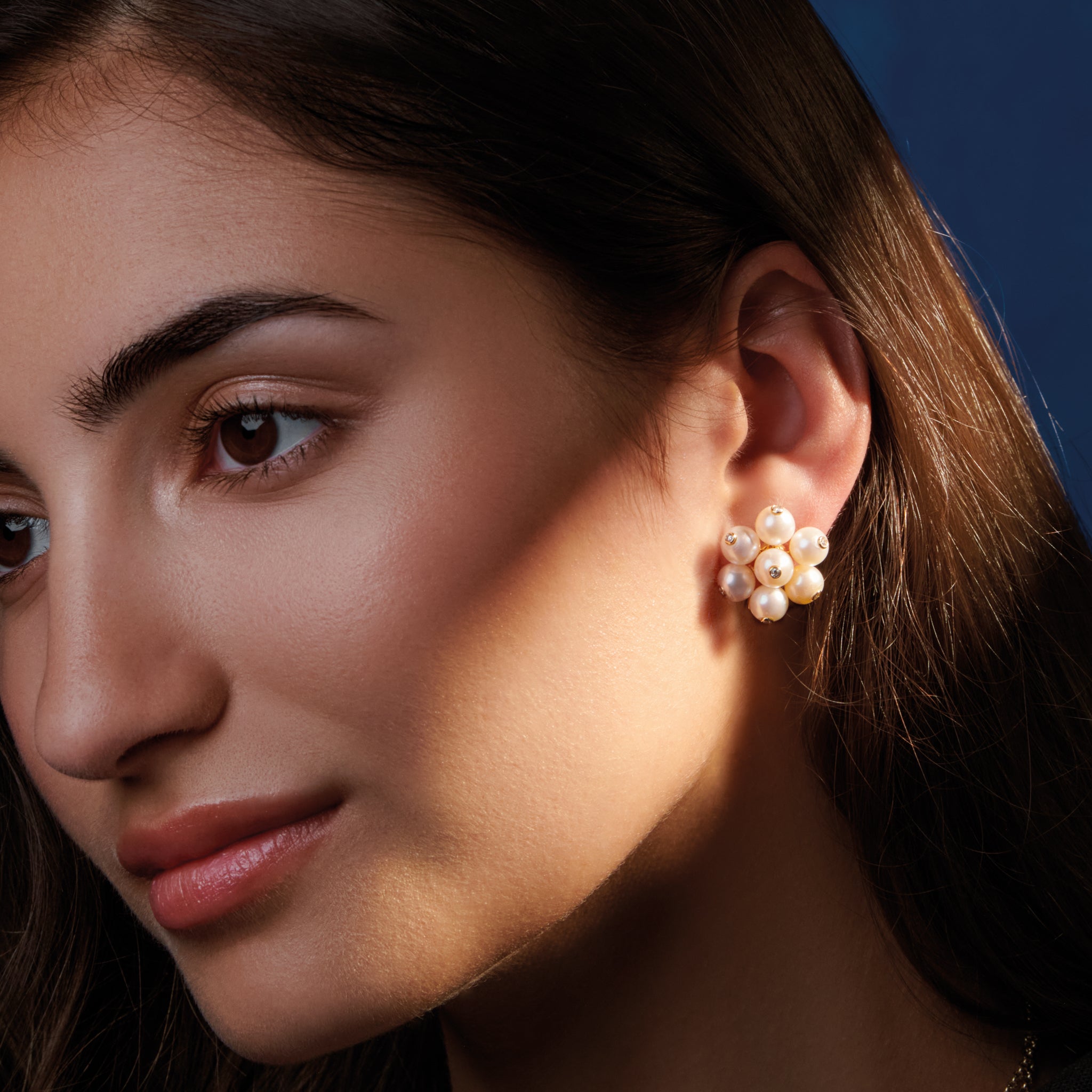 Model wearing handcrafted earrings in 18ct yellow gold featuring a cluster of white pearls. The pearls are interspersed with small diamonds.