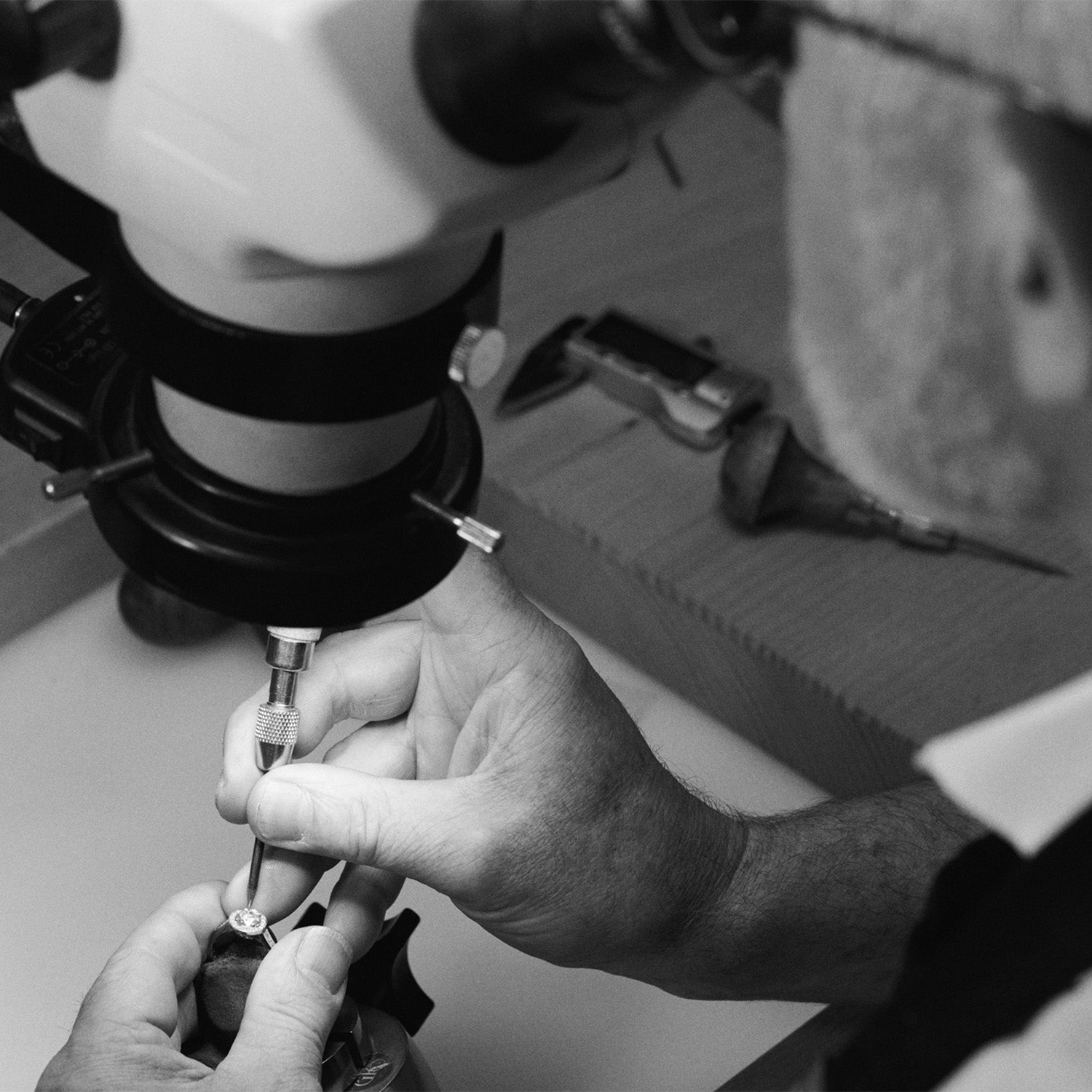 A workshop image showing an artisan setting precious stones in a engagement ring using a setting tool.