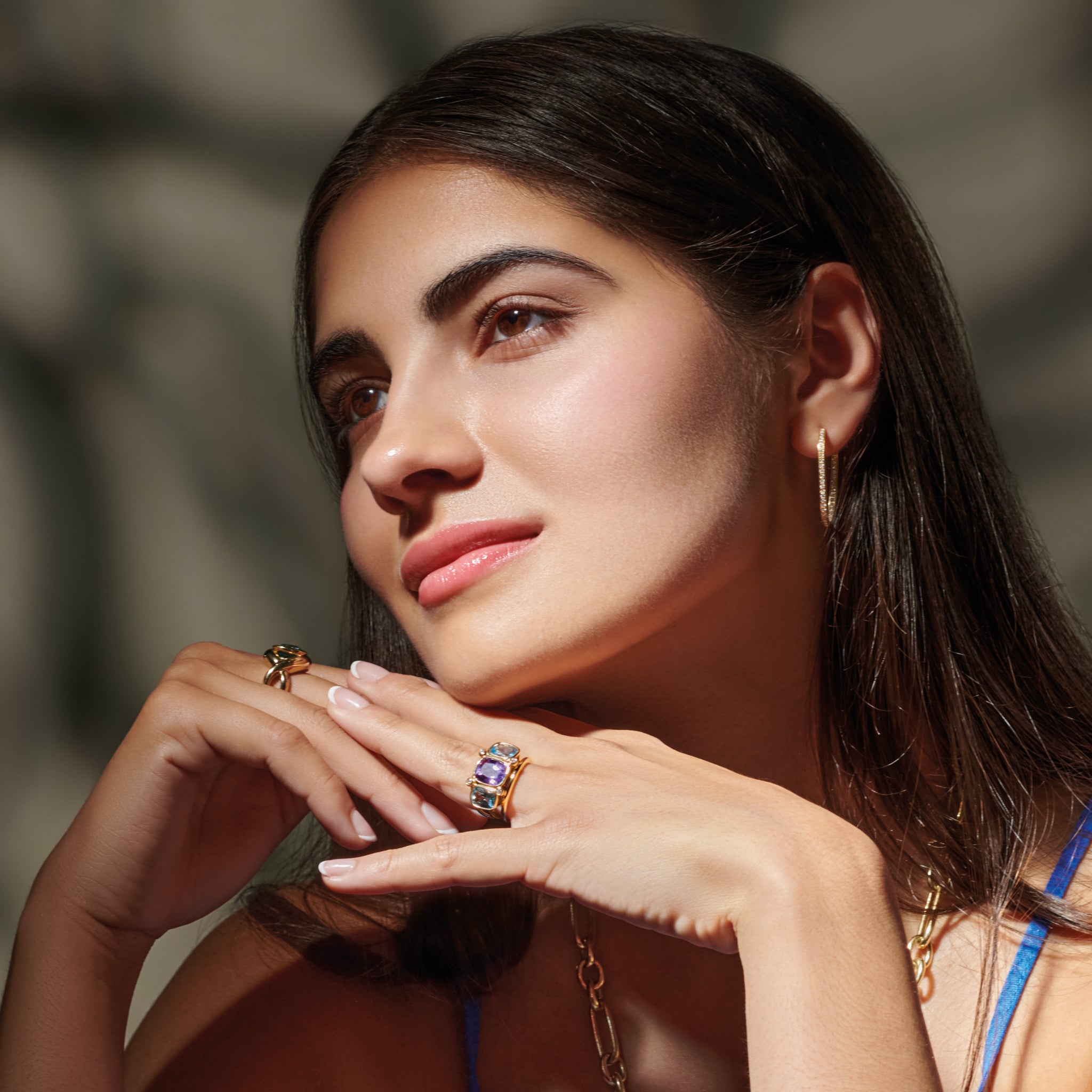 Model wearing a handcrafted 18ct yellow gold ring featuring rectangular shaped amethyst, blue topaz and diamonds.