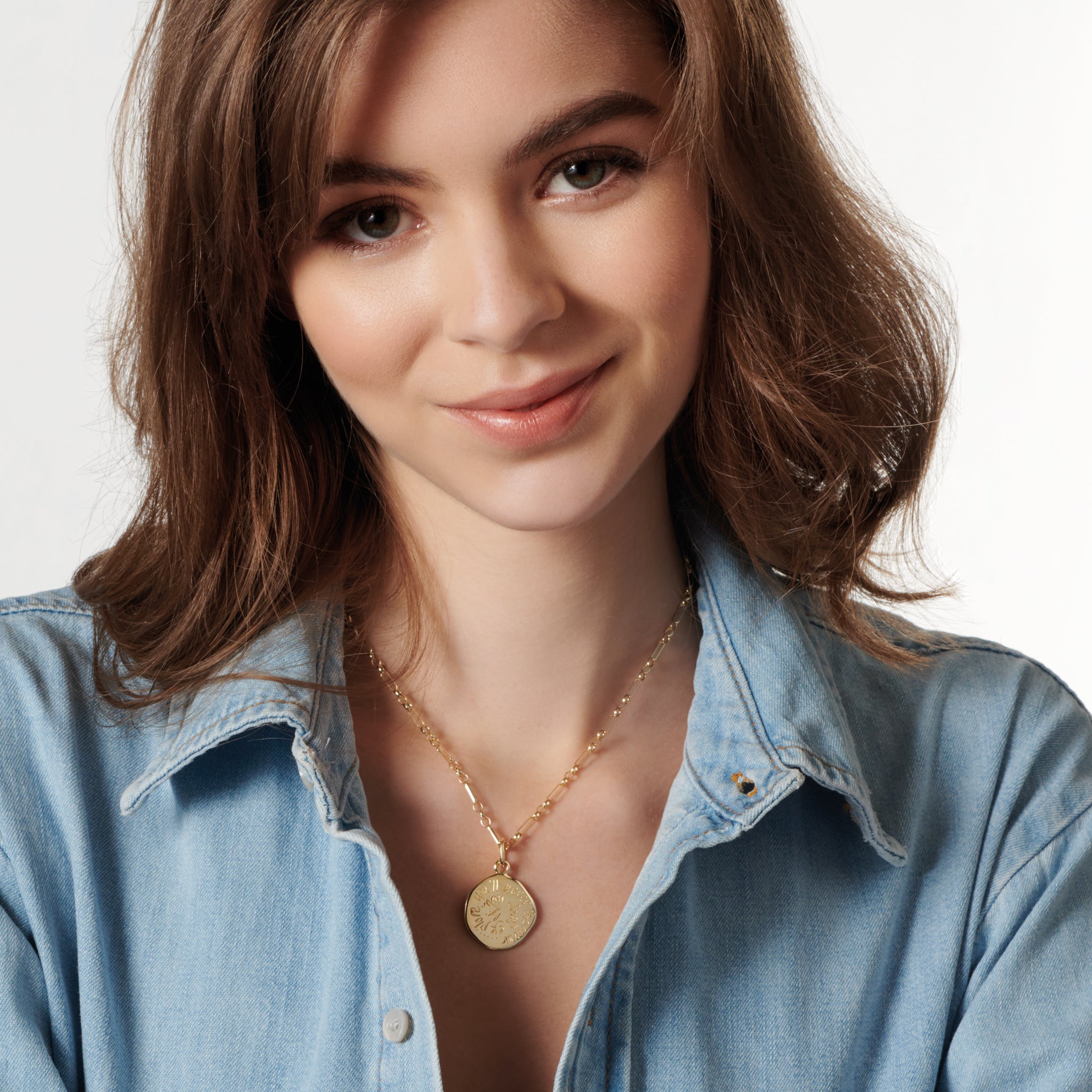 Model wearing a handcrafted round yellow gold necklace pendant engraved with a quote.