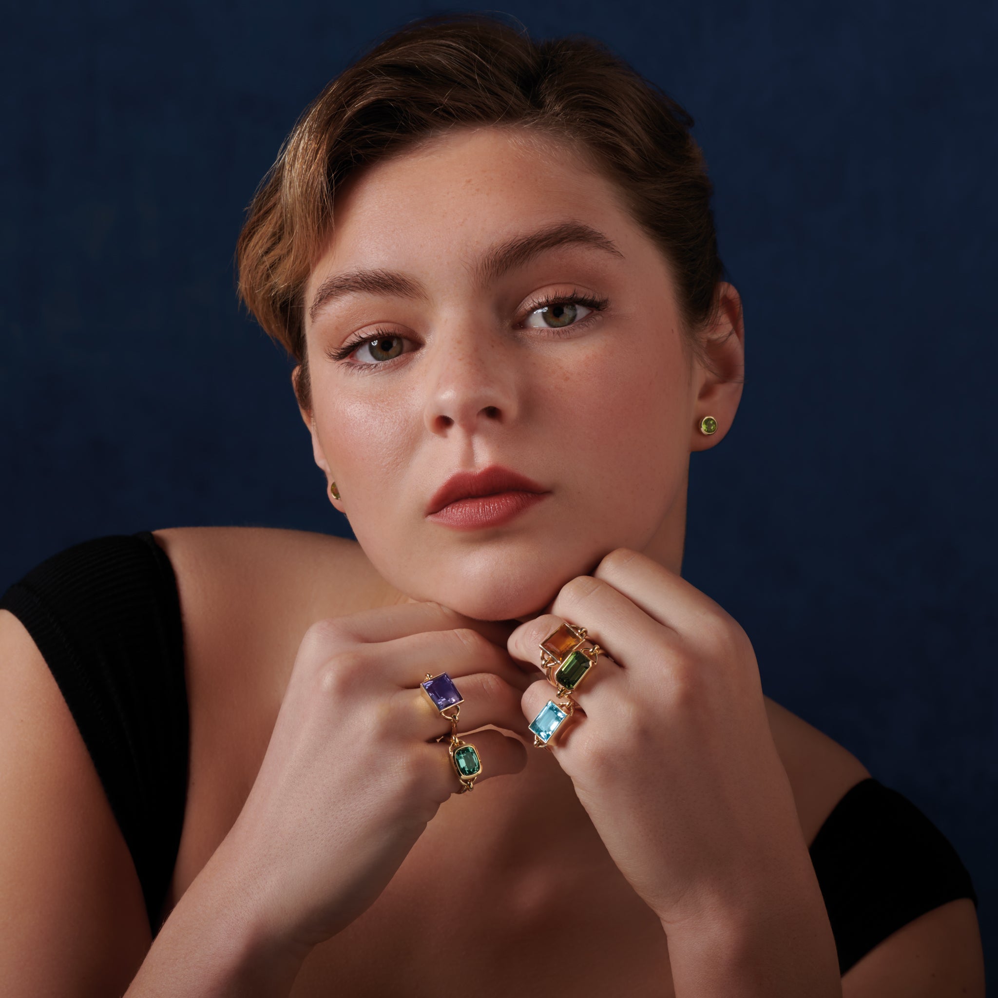 Model wearing handcrafted rings in precious metals featuring central precious stones.