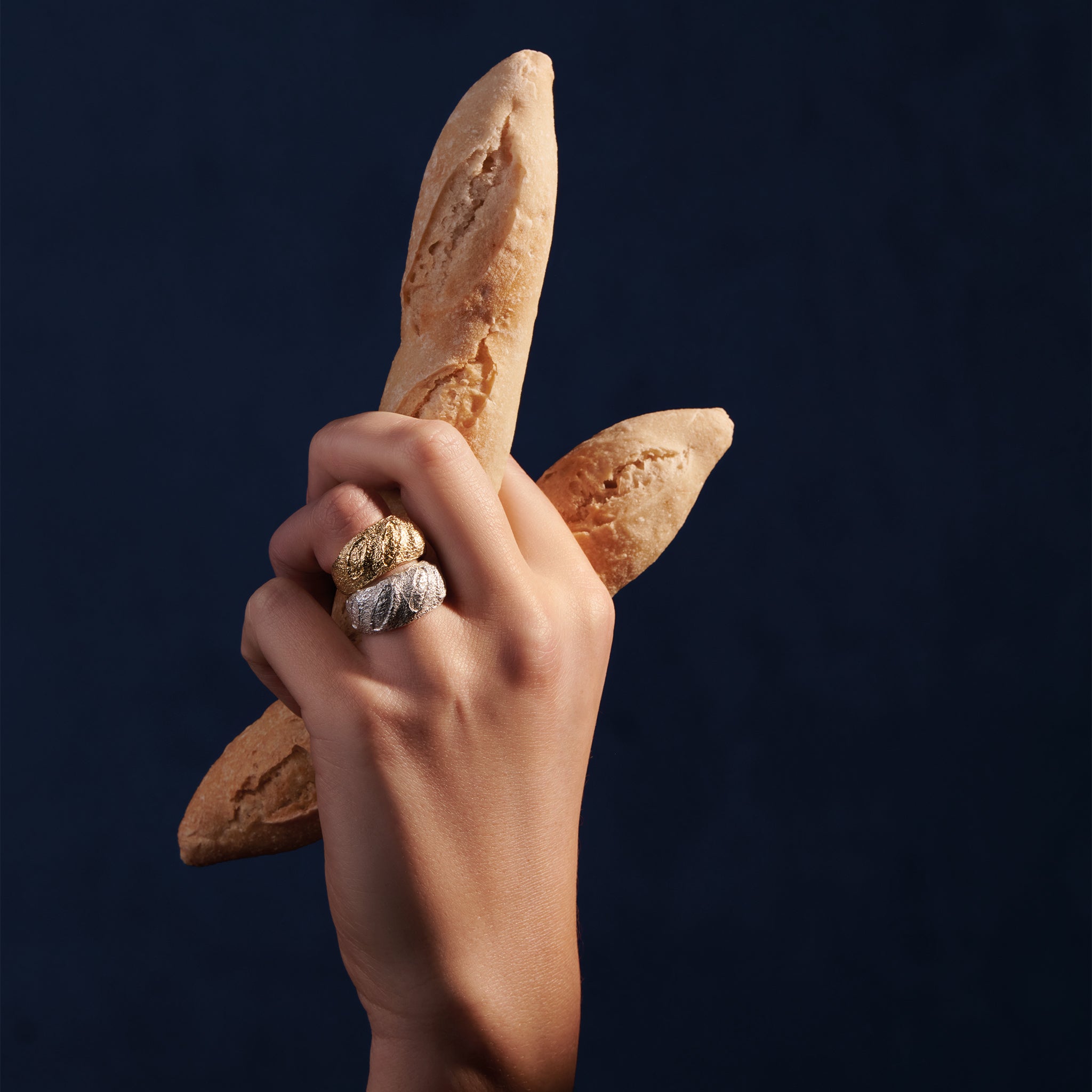 Model wearing handcrafted sterling silver and yellow gold rings designed with the intricate pattern and texture of a French baguette.
