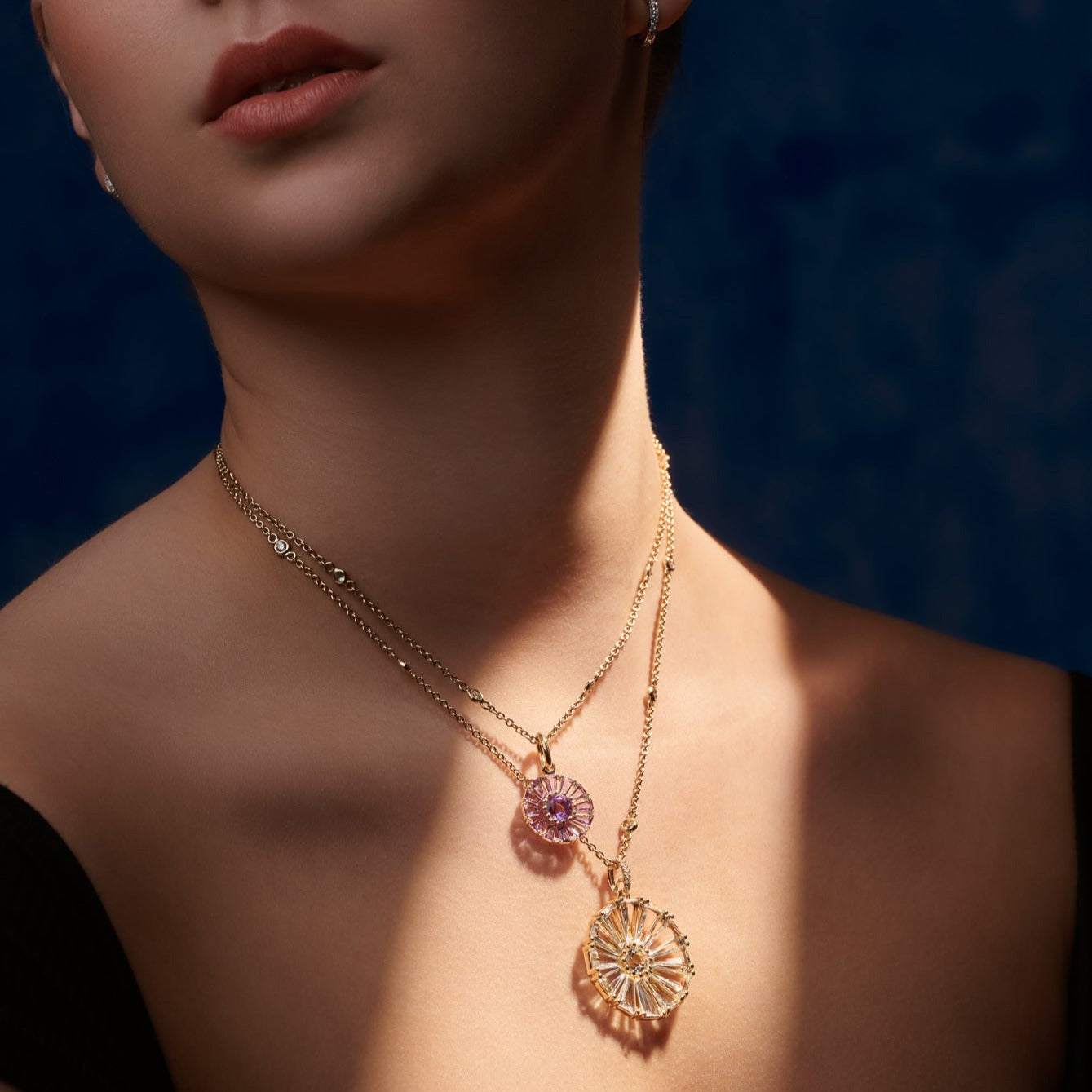 Model wearing two handcrafted necklace pendants in precious metal featuring a circular arrangement of precious stones.