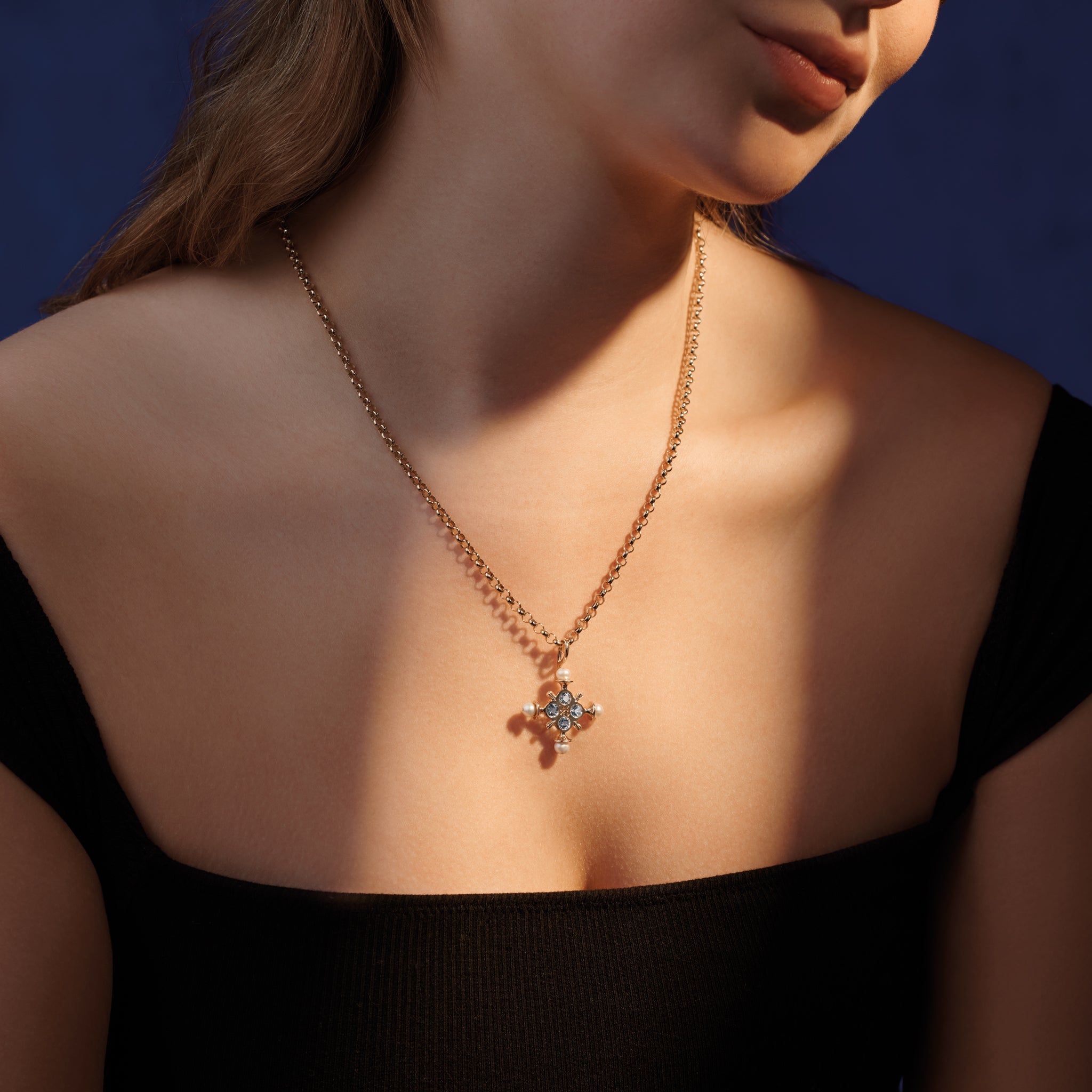 Model wearing a handcrafted cross necklace pendant in precious metal with precious stone.
