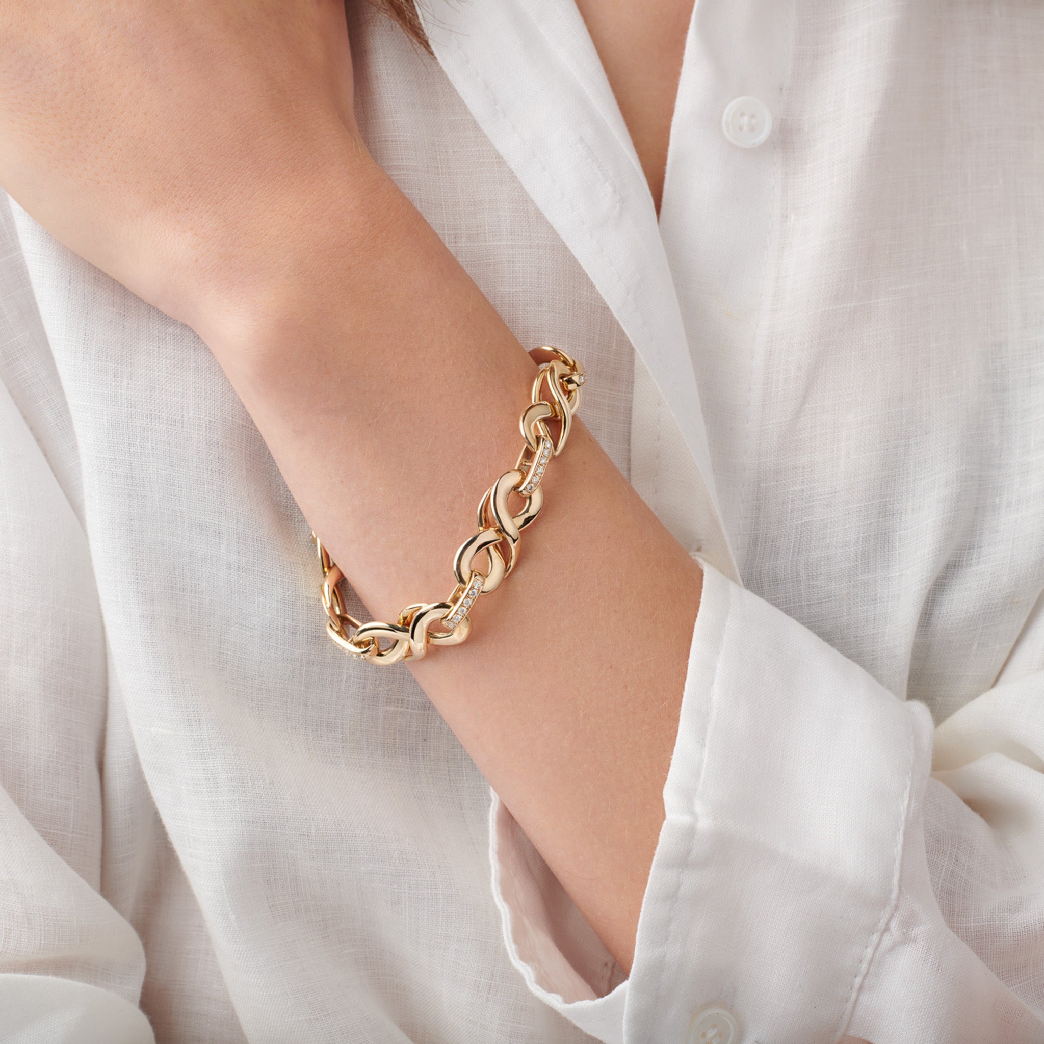 Model wearing a handcrafted yellow gold bracelet featuring 's' shaped links with precious stones.