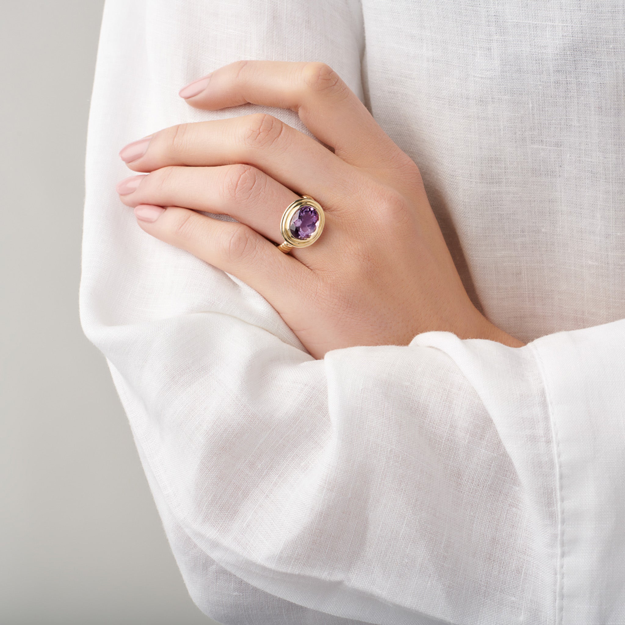 Model wearing a handcrafted ring in precious metal featuring a prominent oval precious stone.