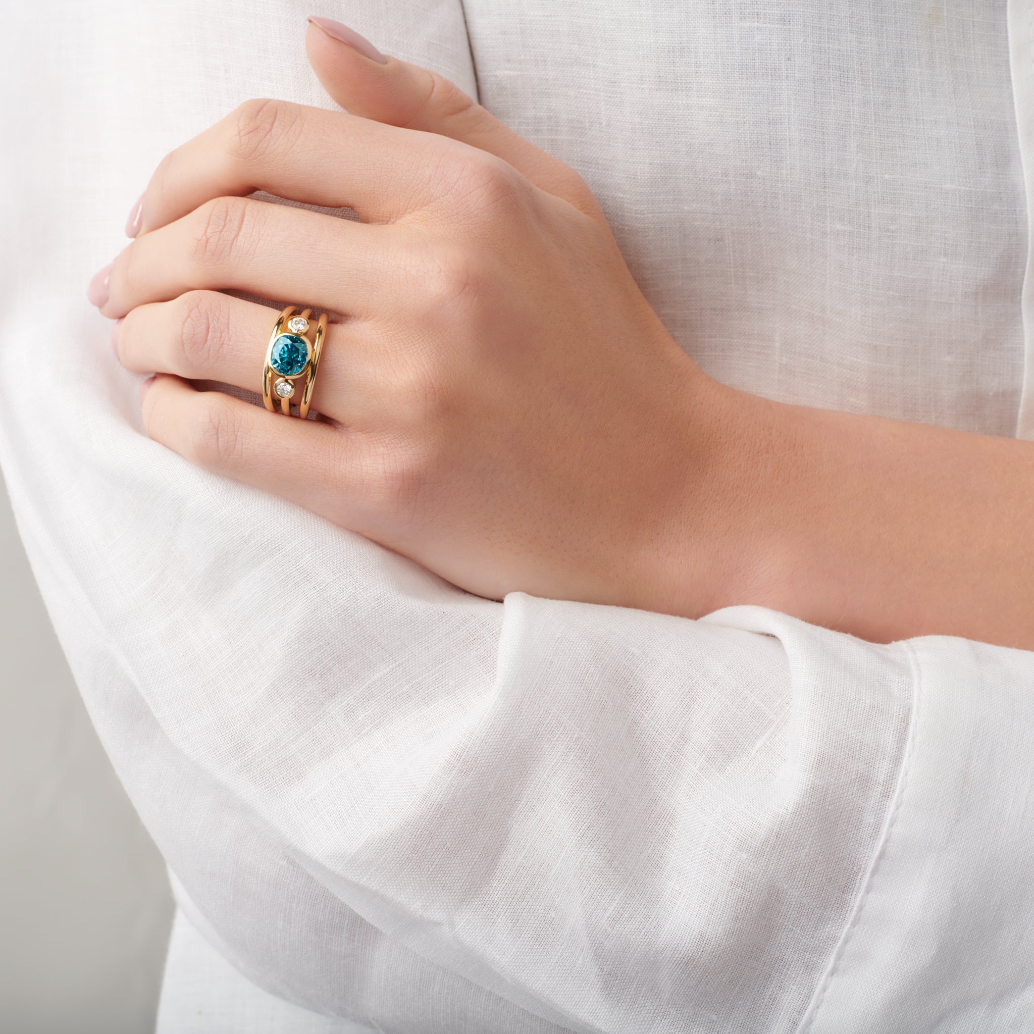 Model wearing a Handcrafted 18ct yellow gold ring with a central precious stone, flanked by two round diamonds.
