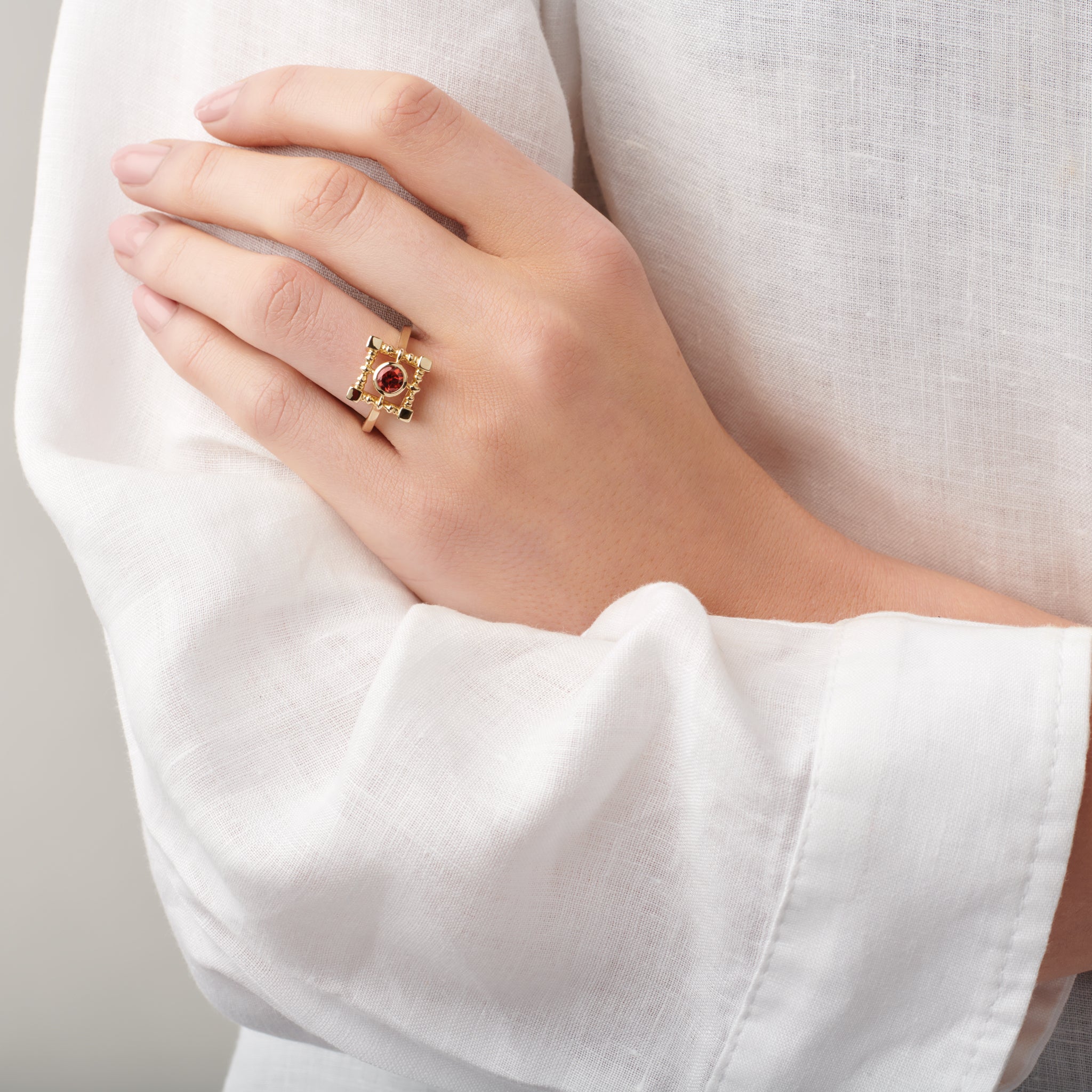Model wearing a handcrafted ring in yellow gold featuring a square-shaped frame with a central garnet gemstone.