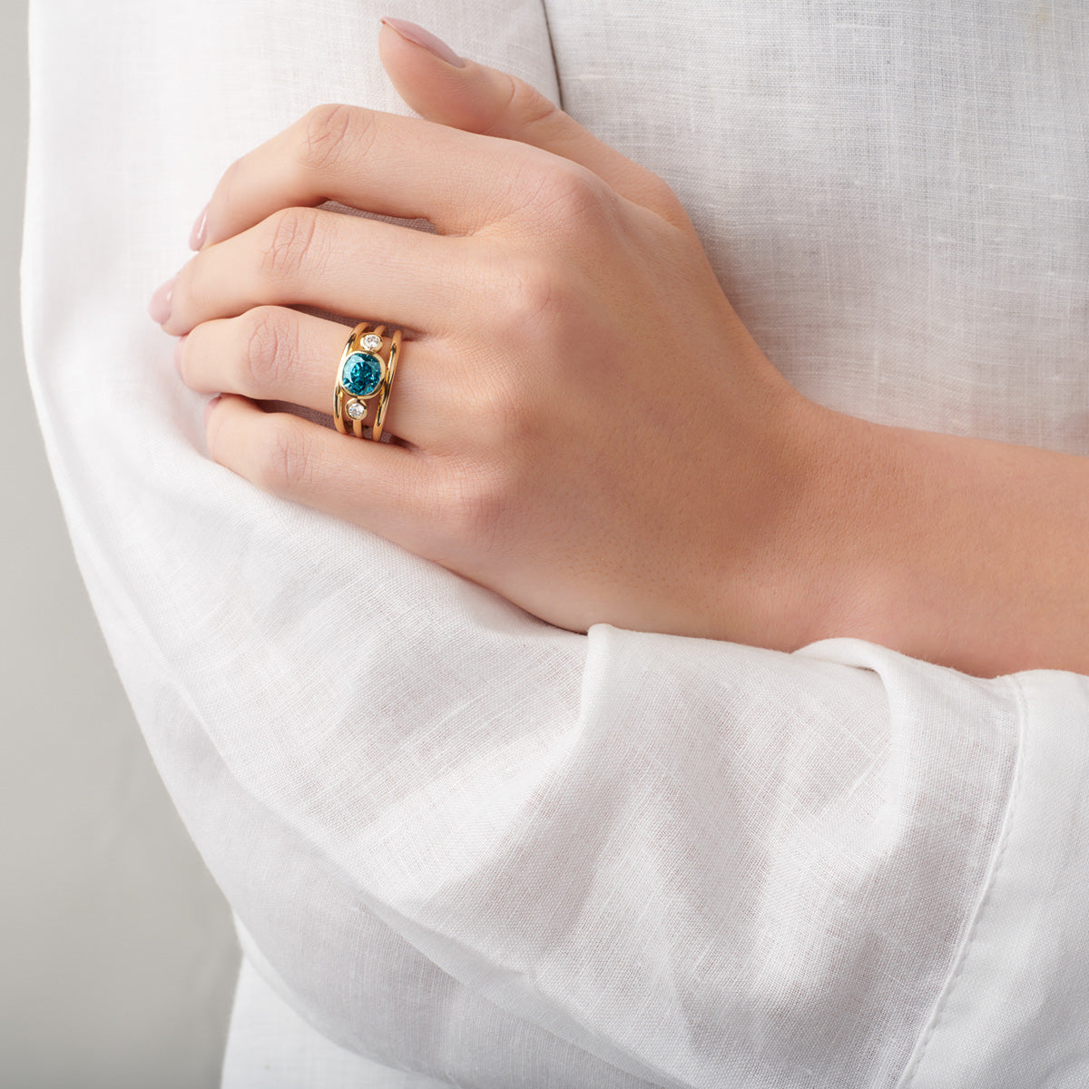 A hand showcasing an 18ct yellow gold ring set with a centre gemstone and diamonds.