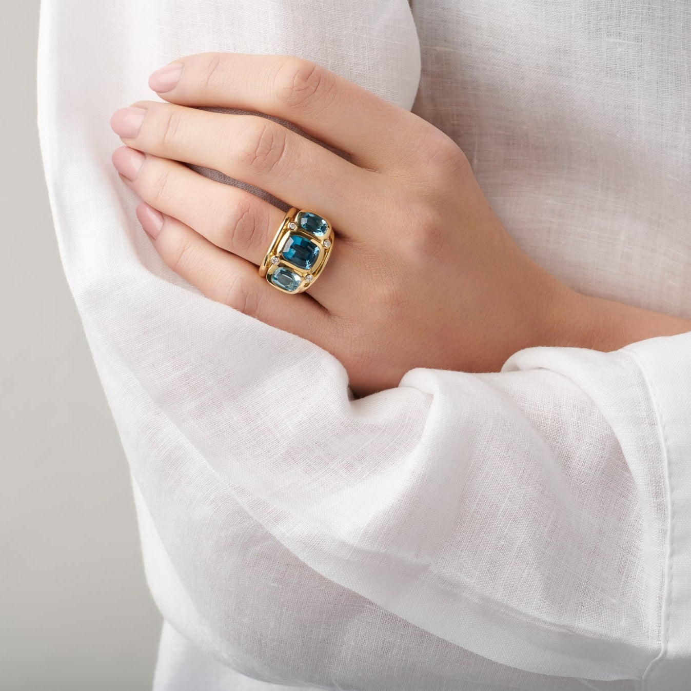 Model wearing a handcrafted 18ct yellow gold ring featuring rectangular shaped blue topaz and diamonds.