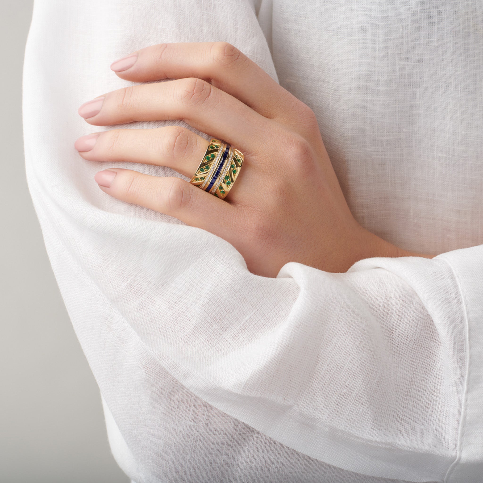 Model wearing a handcrafted 18ct yellow gold ring featuring sapphires, emeralds and diamonds.