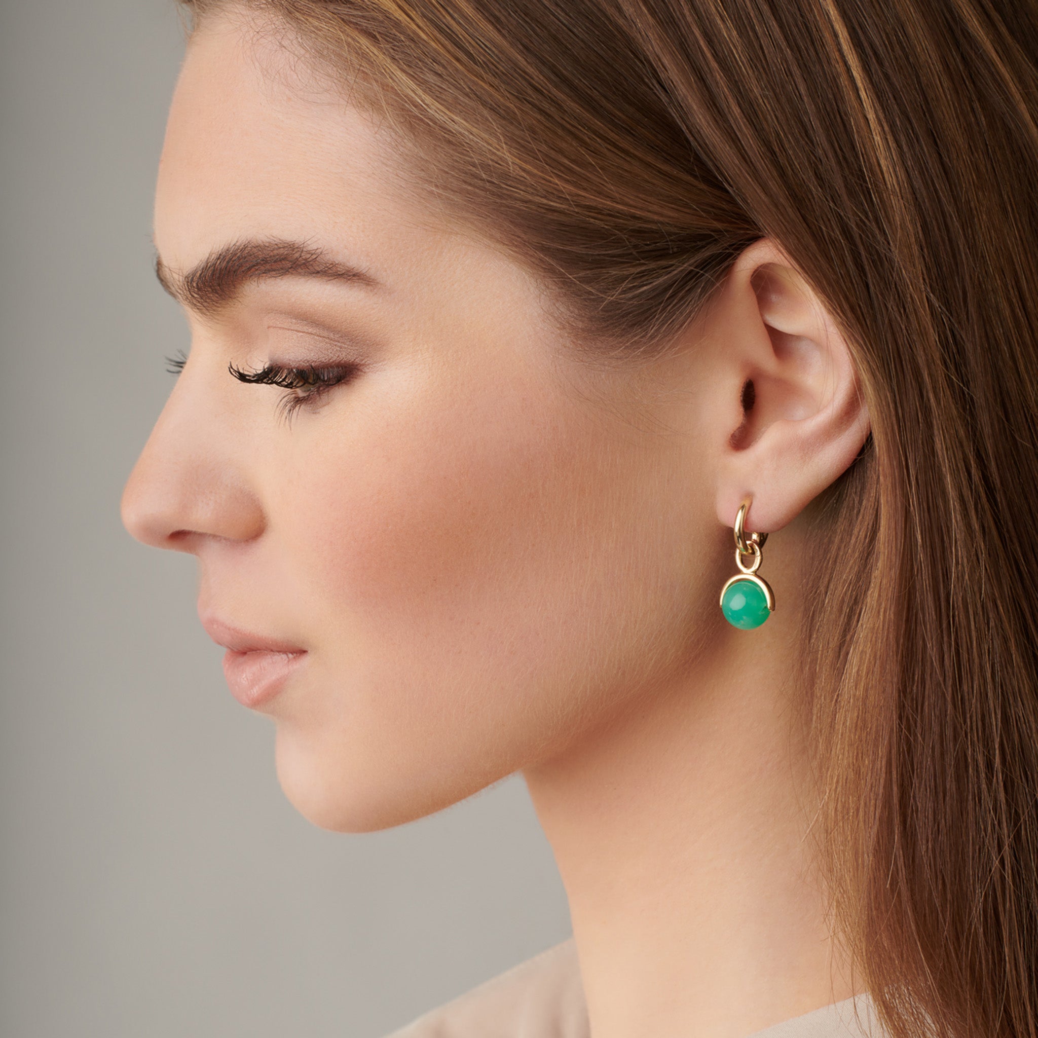 Model wearing handcrafted earring drops in precious metal featuring round precious stones.