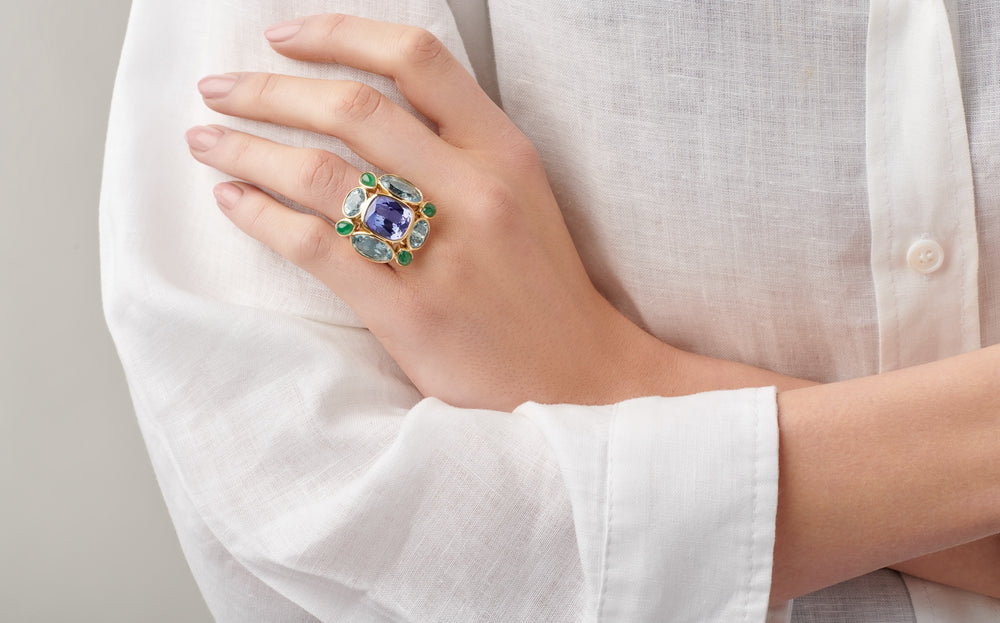 Model wearing a handcrafted yellow gold ring featuring tanzanite and precious gemstones for the birthstones of December.