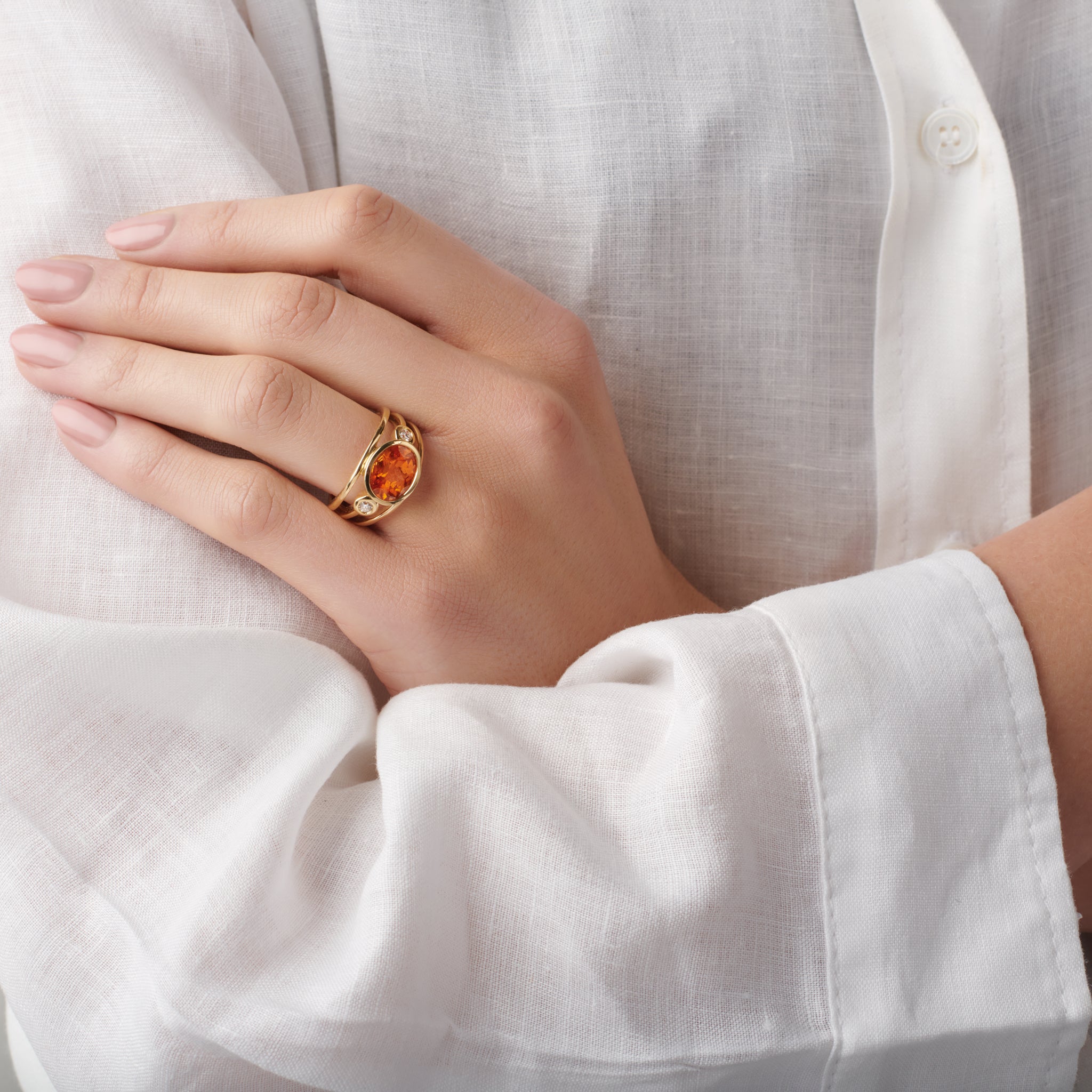 Model wearing a handcrafted ring in precious metal with a central precious stone, flanked by two round diamonds.