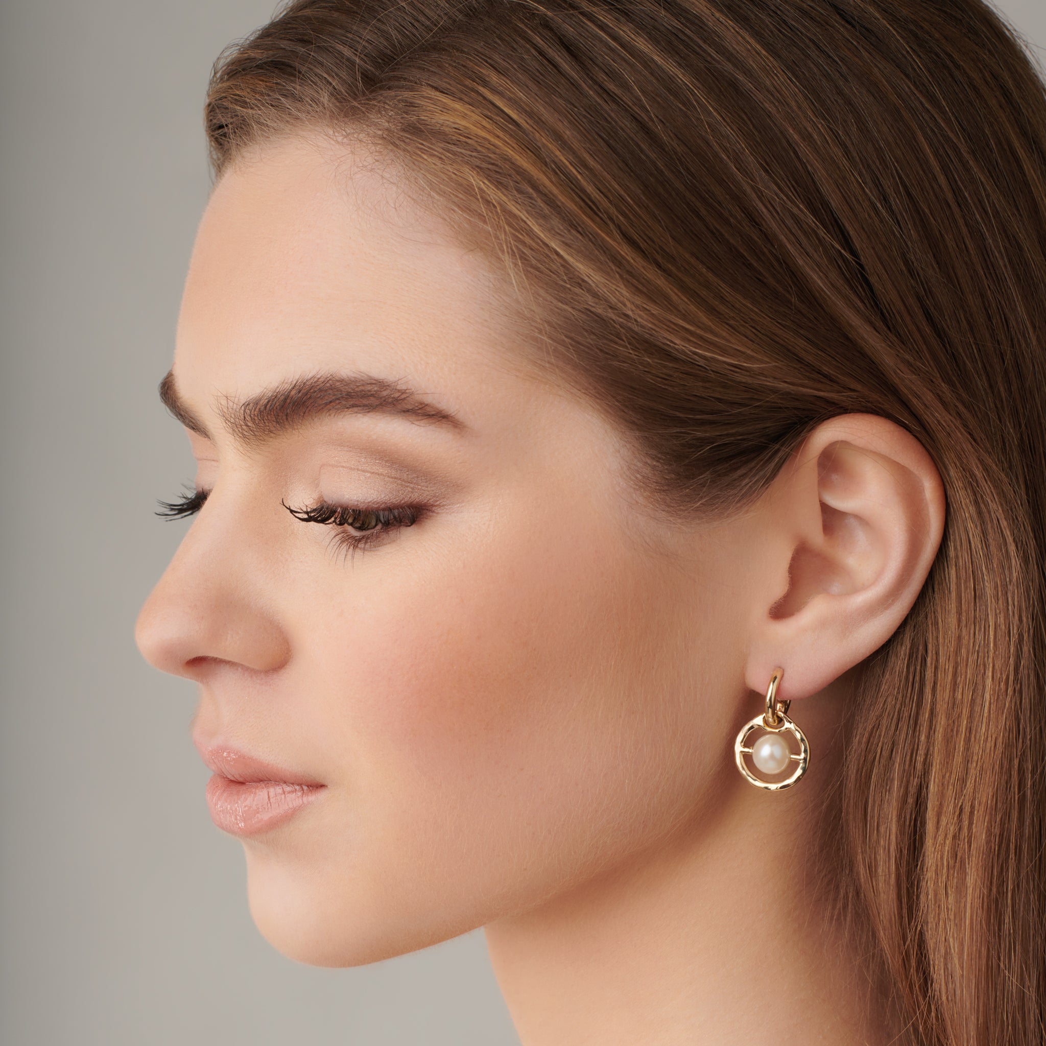 Model wearing handcrafted earring drops in precious metal featuring a round precious stone held within a circle.