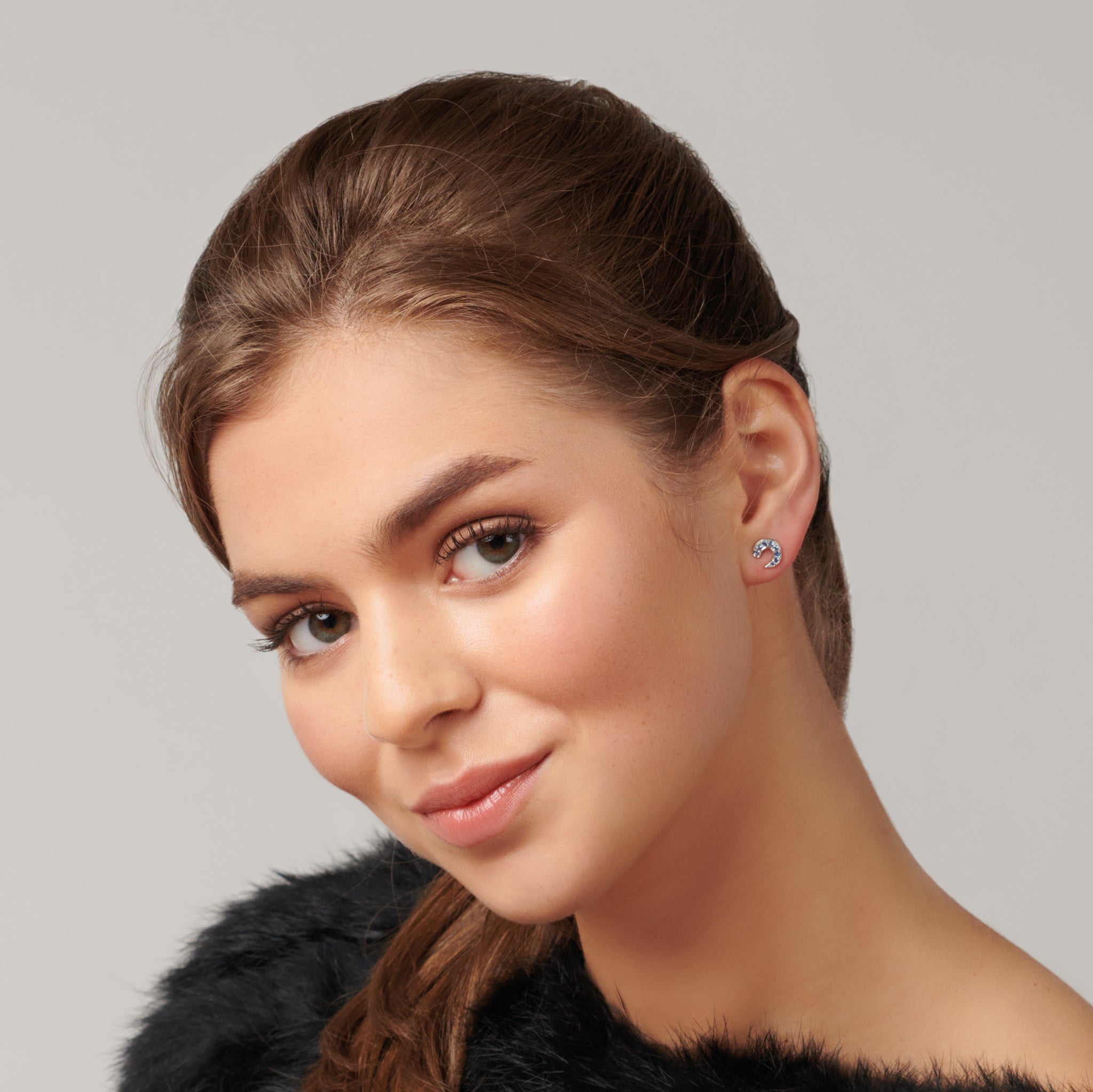 Model wearing handcrafted stud earrings in precious metal featuring a crescent shape with precious stone pav?.