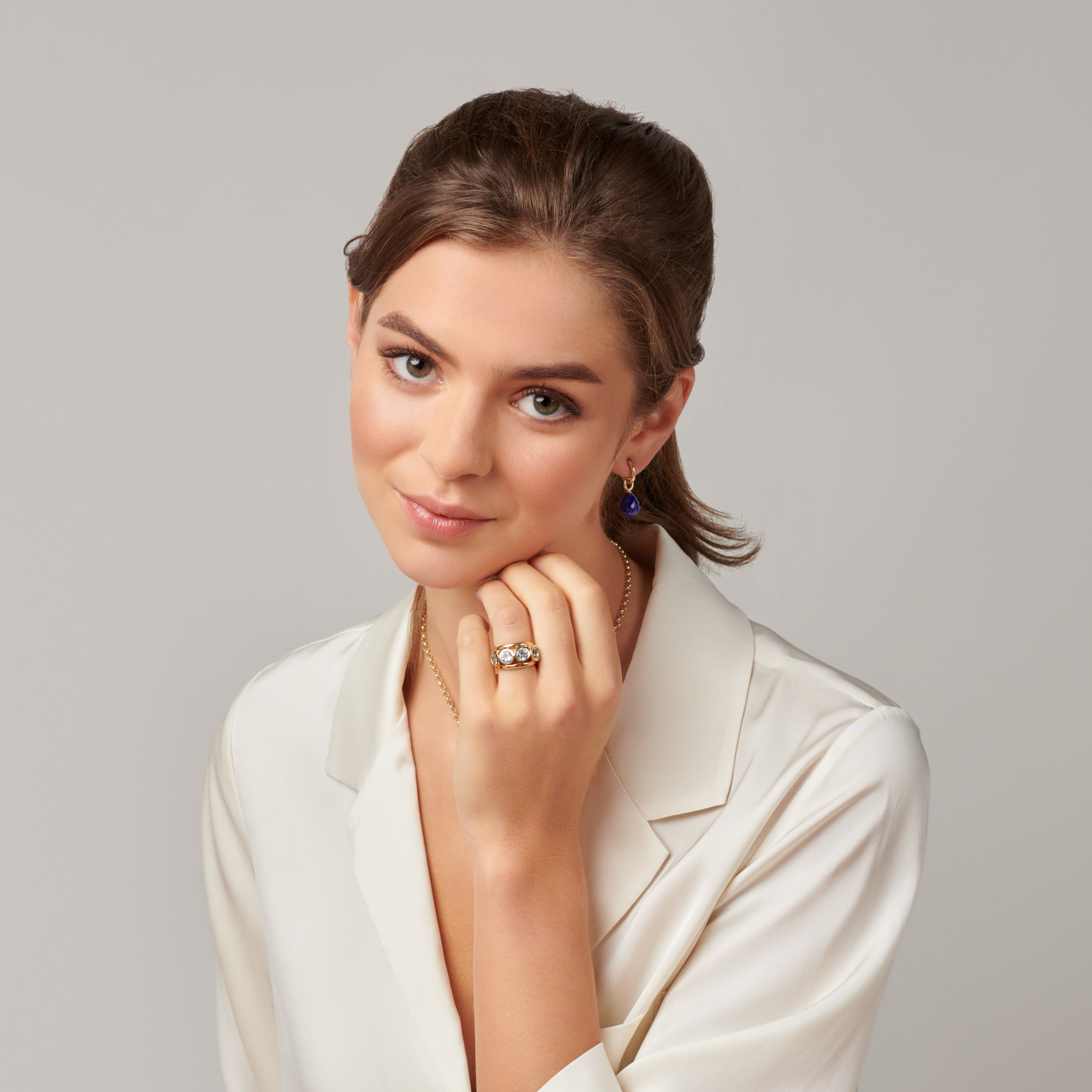 Model wearing a handcrafted ring in precious metal with a bold band and five circular precious stones in bezel settings.