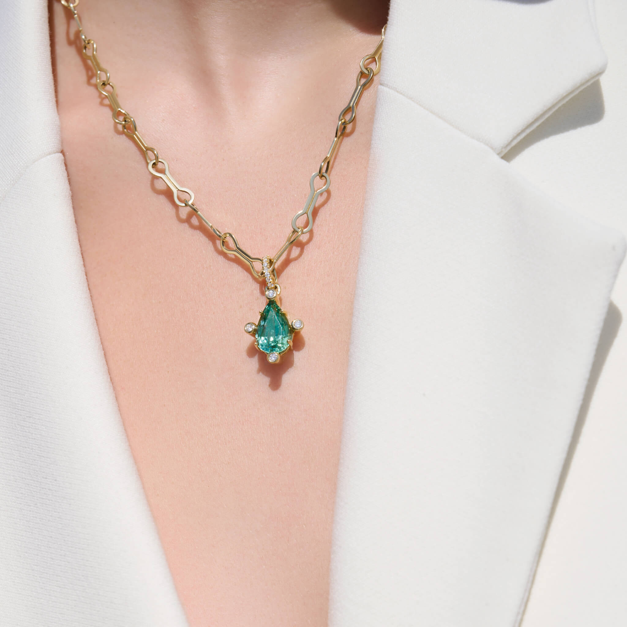 Model wearing handcrafted 18ct yellow gold pendant with pear facetted green gemstone set with four diamonds. on gold chain with diamonds.