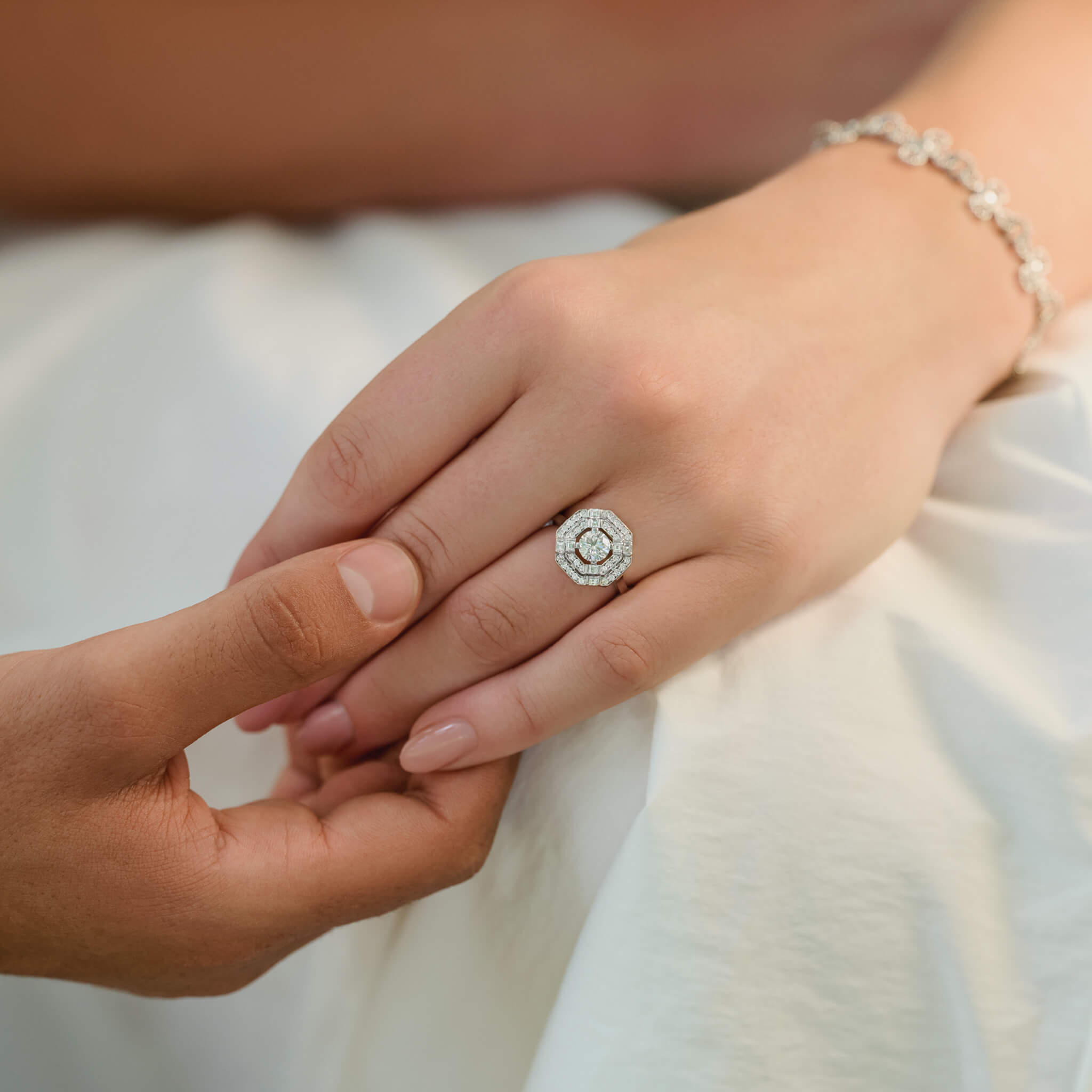 Model wearing a 18ct white gold engagement ring featuring a central square-cut central diamond, surrounded by two tiers of small round diamonds set in a hexagonal pattern.