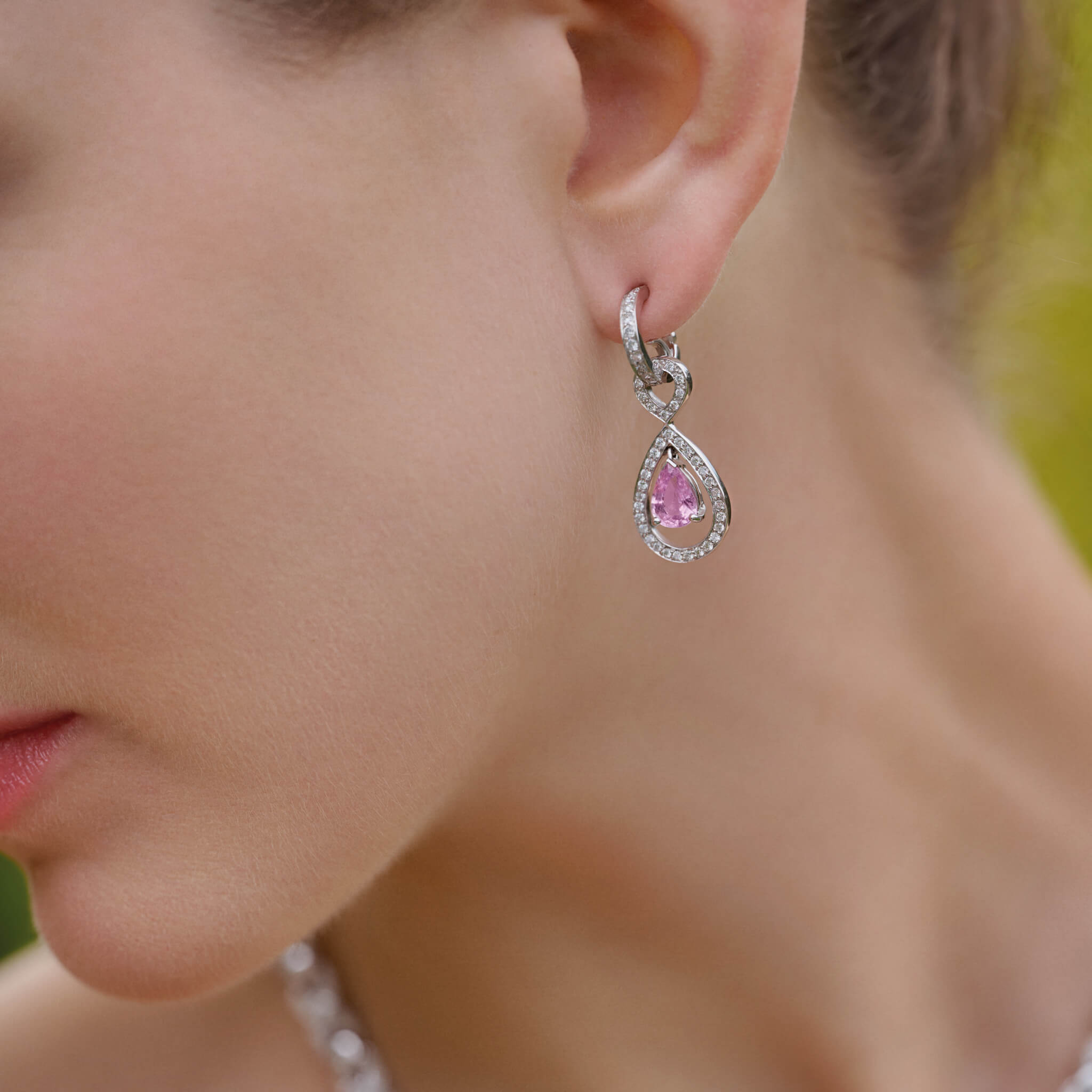 Model wearing handcrafted 18ct white gold earring drops featuring a central pink sapphire surrounded by diamonds.