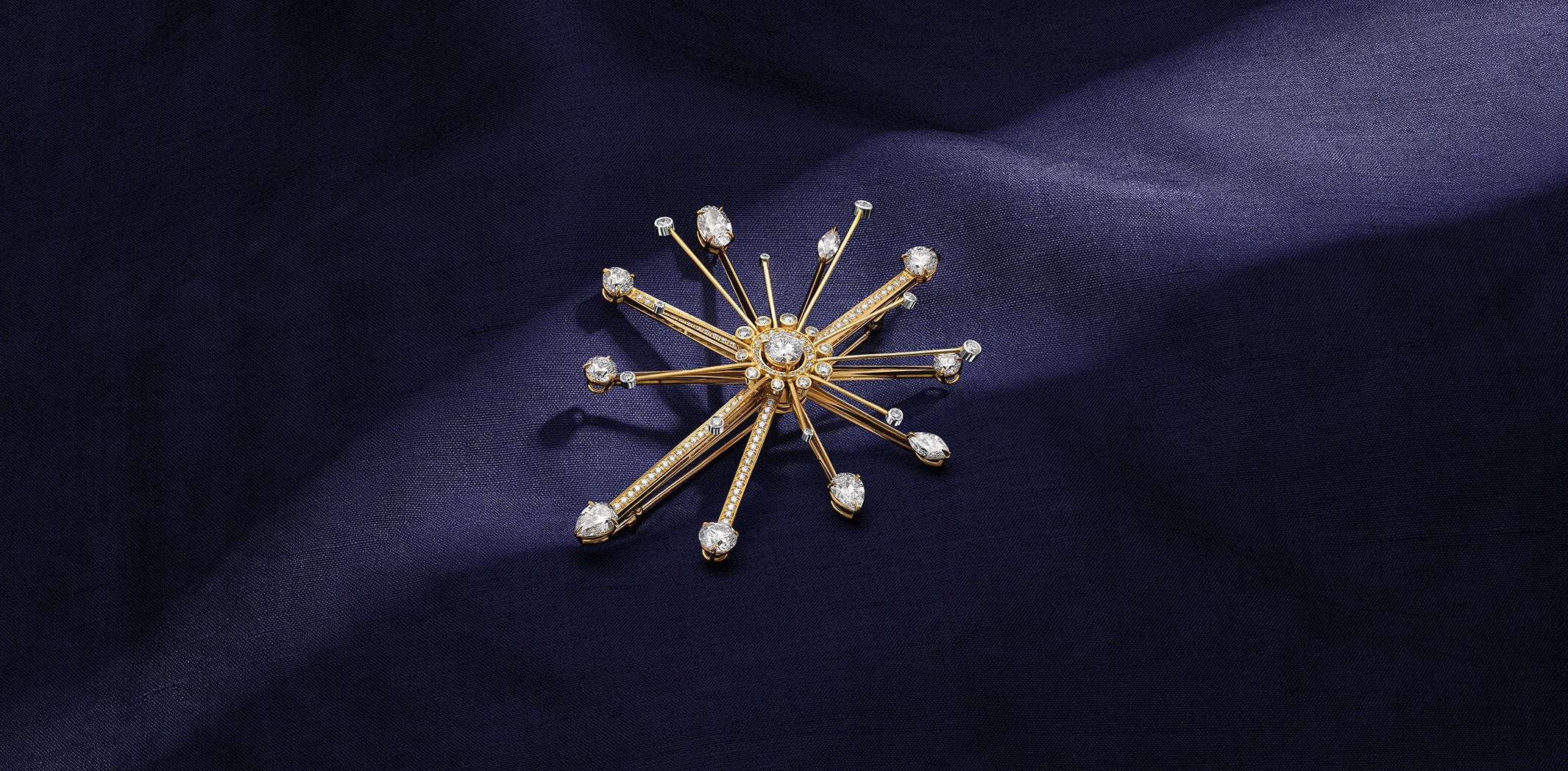 Firework Brooch on a blue fabric background. Made of yellow gold and diamonds