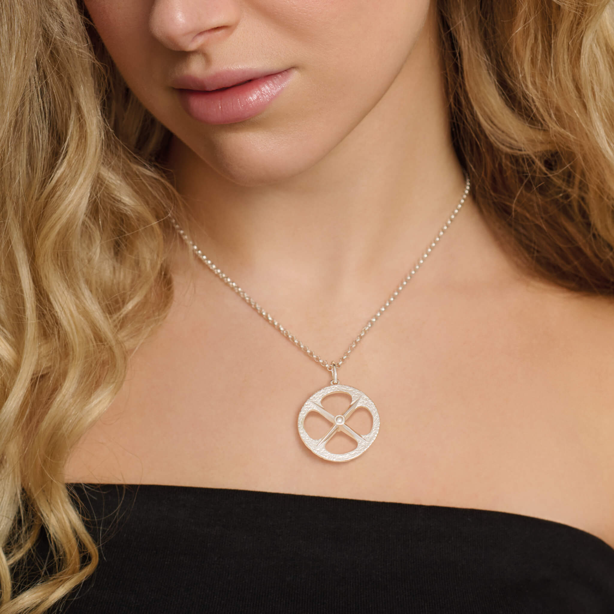 Model wears handcrafted sterling silver large necklace pendant with a circular motif and a cross in the middle.