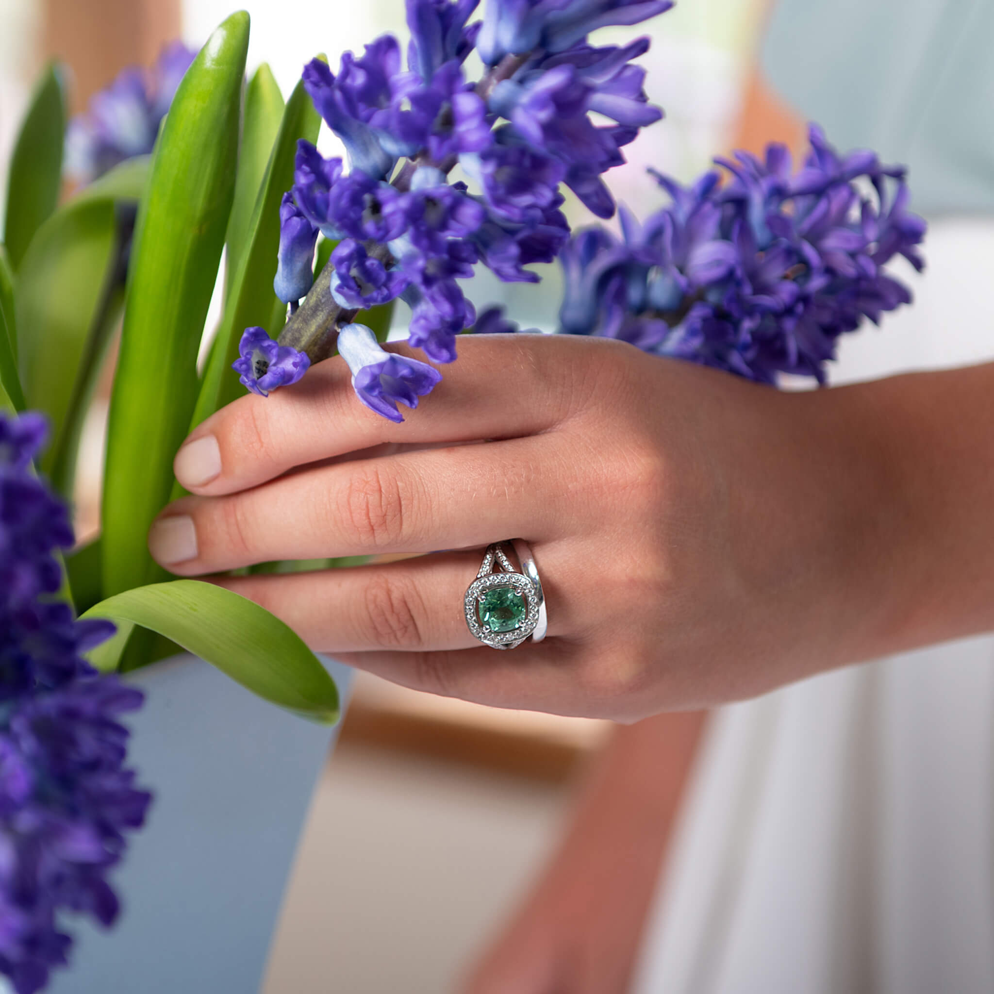 Model wearing a handcrafted 18ct white gold engagement ring featuring a large, mint tourmaline surrounded by a halo of small diamonds and smaller diamonds embedded along the band.