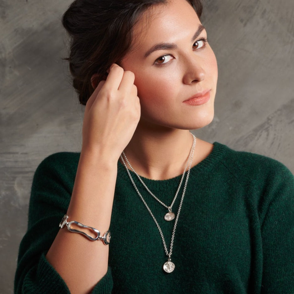 Model wearing a handcrafted sterling silver bracelet featuring the outlines of french paisteries: ?clair, canel?, pain au chocolat and croissant.