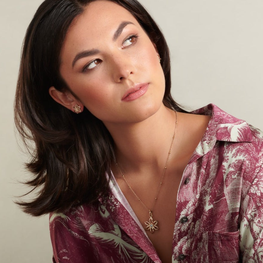 Model wearing a handcrafted flower necklace pendant in precious metal with a central precious stone.