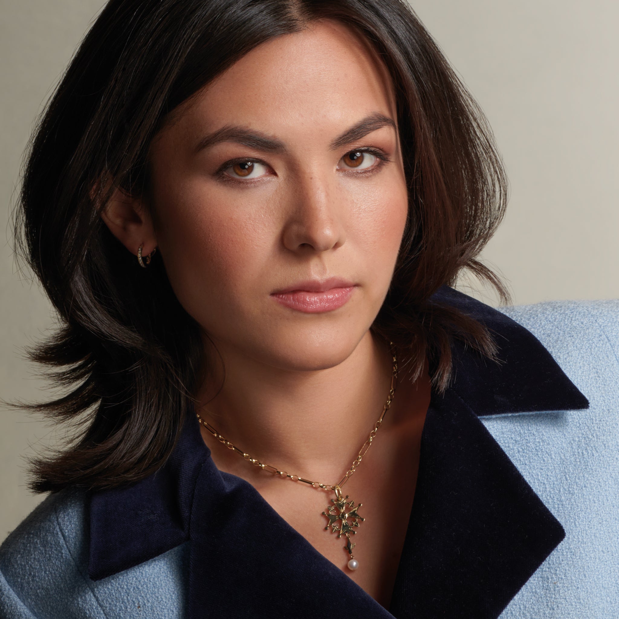 Model wearing a handcrafted yellow gold Huguenot cross pendant with pearl, birthstone of June.