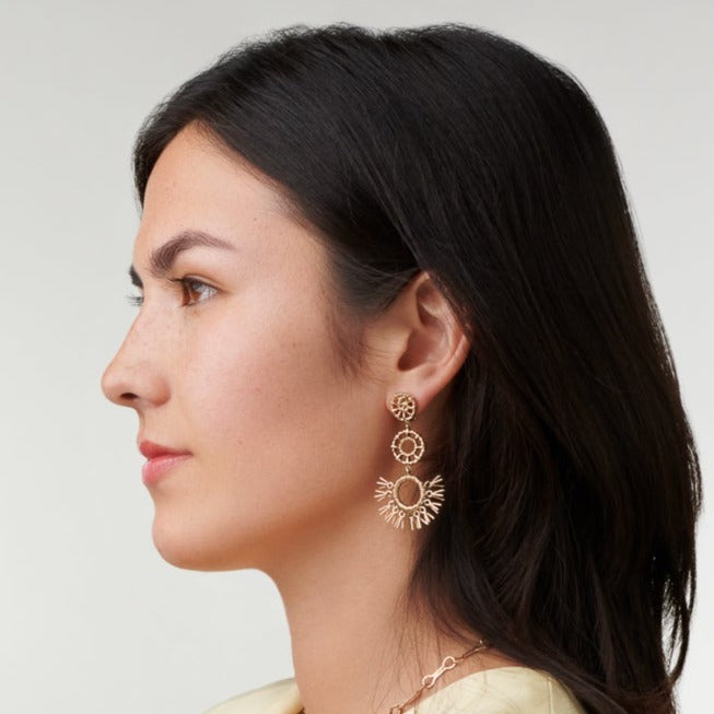 Model wearing handcrafted yellow gold earrings in the shape of dried palm fronds from Morocco.