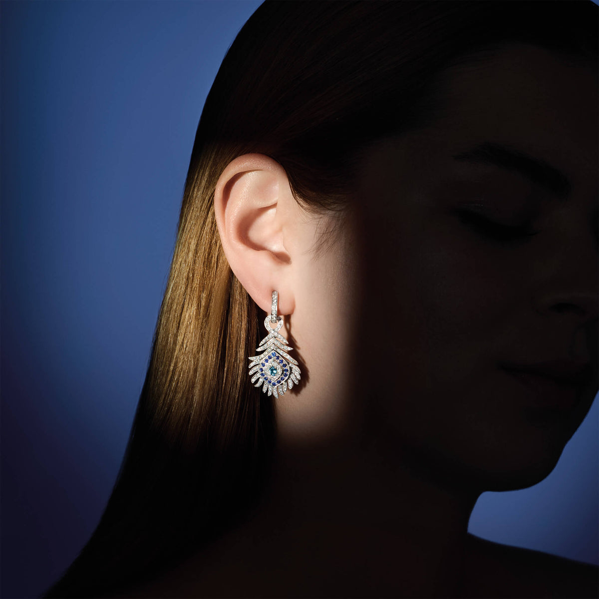 Model wearing handcrafted high jewellery Peacock occasion earrings in white gold with diamond and sapphire