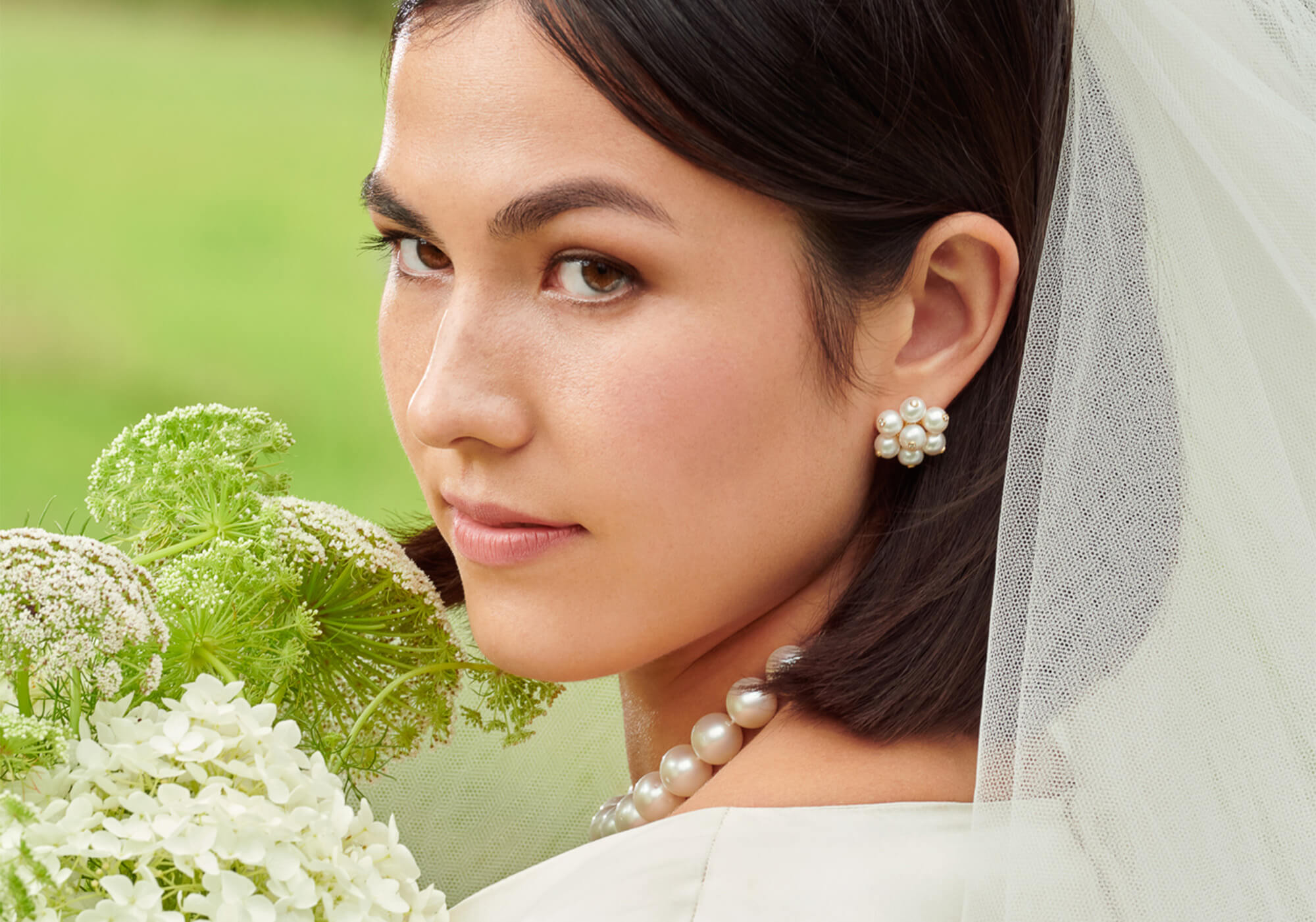 Bride wearing a pearl necklace and earrings, holding a bouquet of white flowers.
