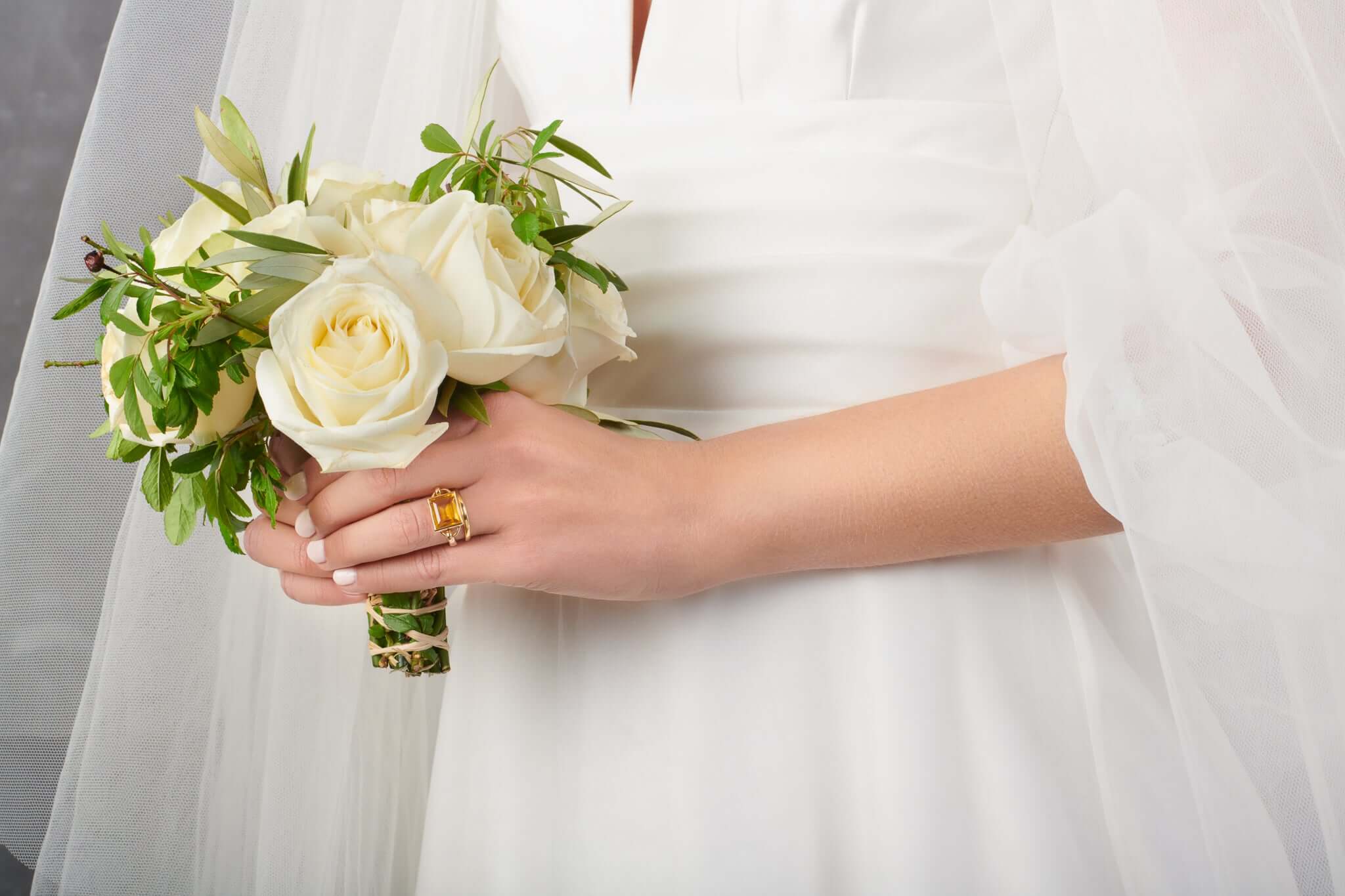 Model wearing a wedding dress and a handcrafted yellow gold ring featuring a baguette cut citrine, the perfect contemporary engagement ring.