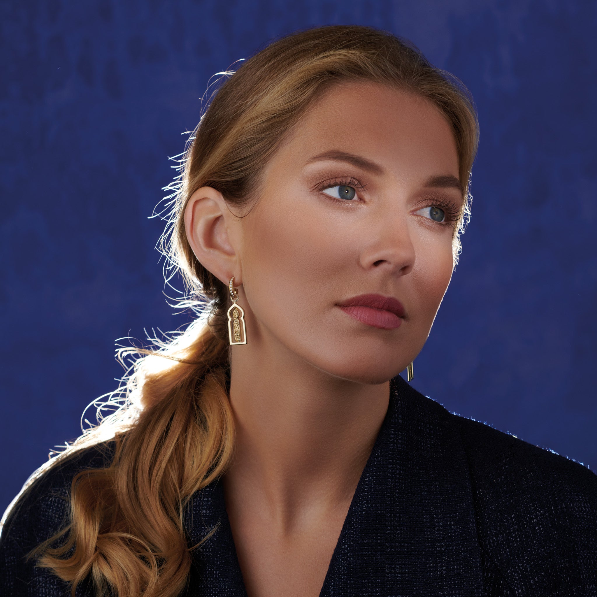 Model wearing handcrafted yellow gold earring drops featuring a narrow door with diamonds.