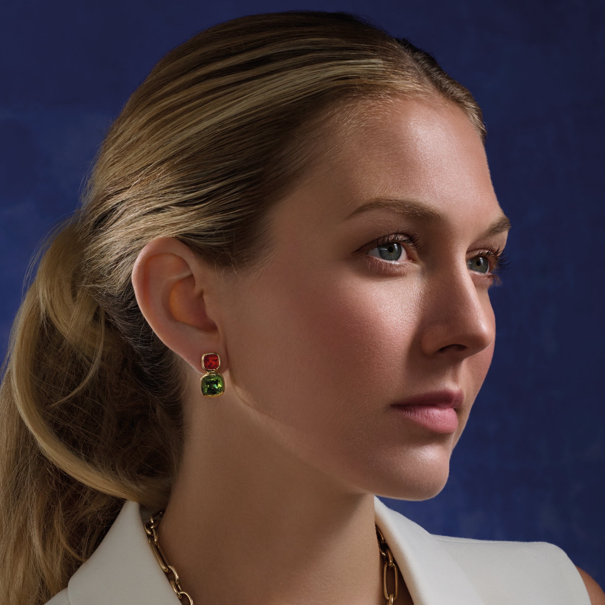 Model wearing handcrafted 18ct yellow gold square shaped earrings featuring fire opal and peridot gemstones.