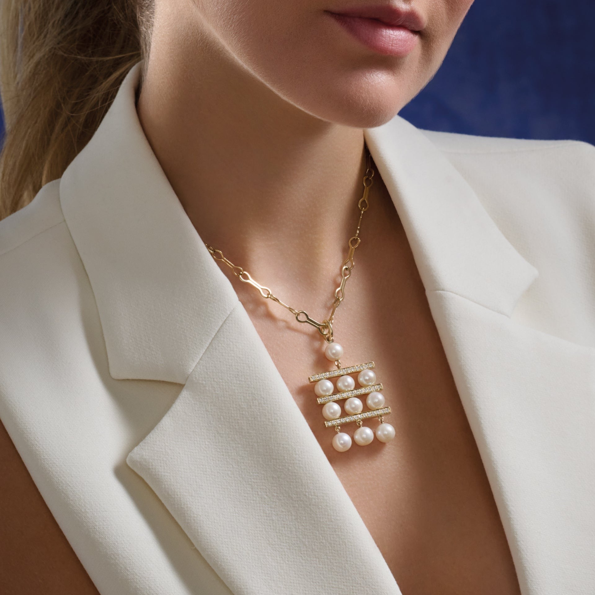 Model wearing a handcrafted yellow gold necklace pendant with three tiers of pearls separated by delicate gold lines adorned with diamond pavé.