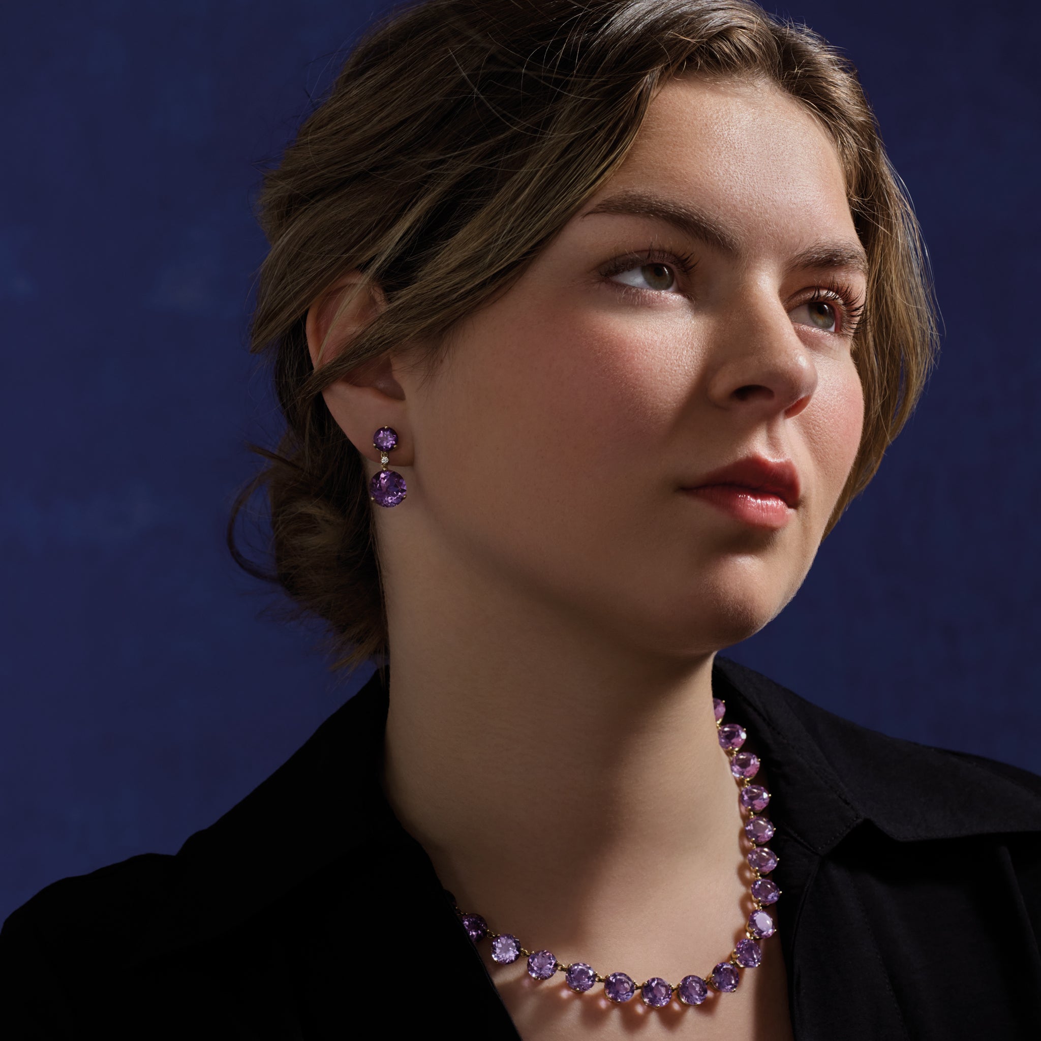 Model wearing handcrafted yellow gold earrings featuring circular amethyst gemstones and diamonds and a yellow gold necklace featuring circular amethyst gemstones.
